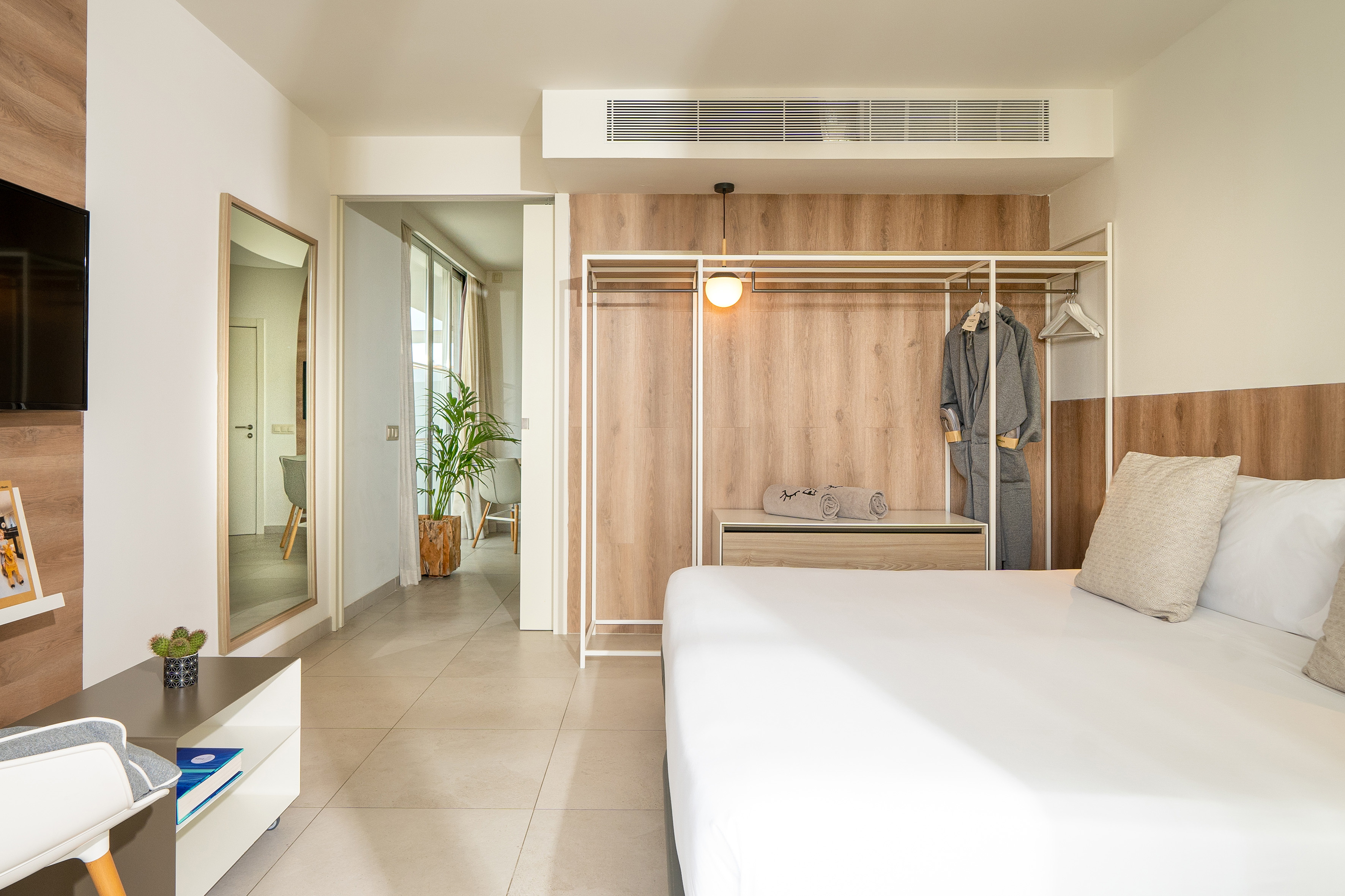 Modern hotel bedroom with white bed, wood paneling, open closet, tiled floor.
