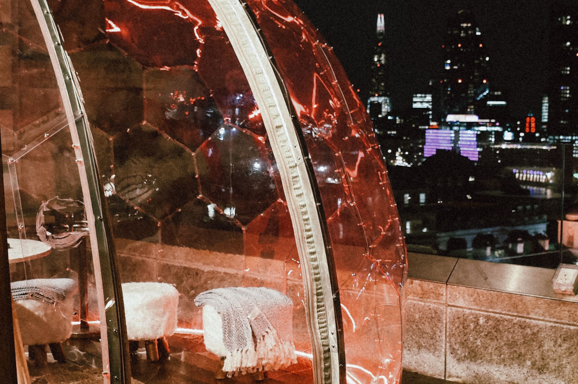 A woman stands on a balcony, with the city skyline stretching out behind her.