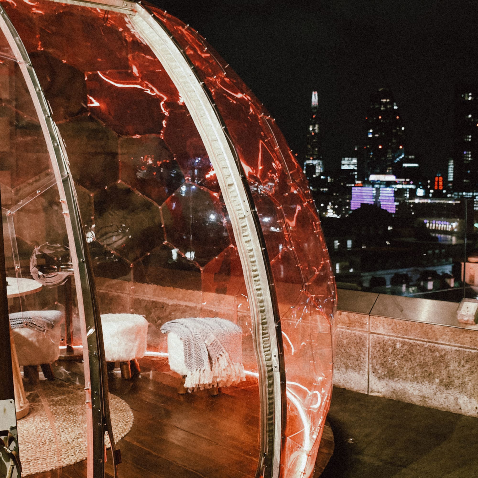 A glass dome sits on a rooftop, featuring a table and chairs inside.