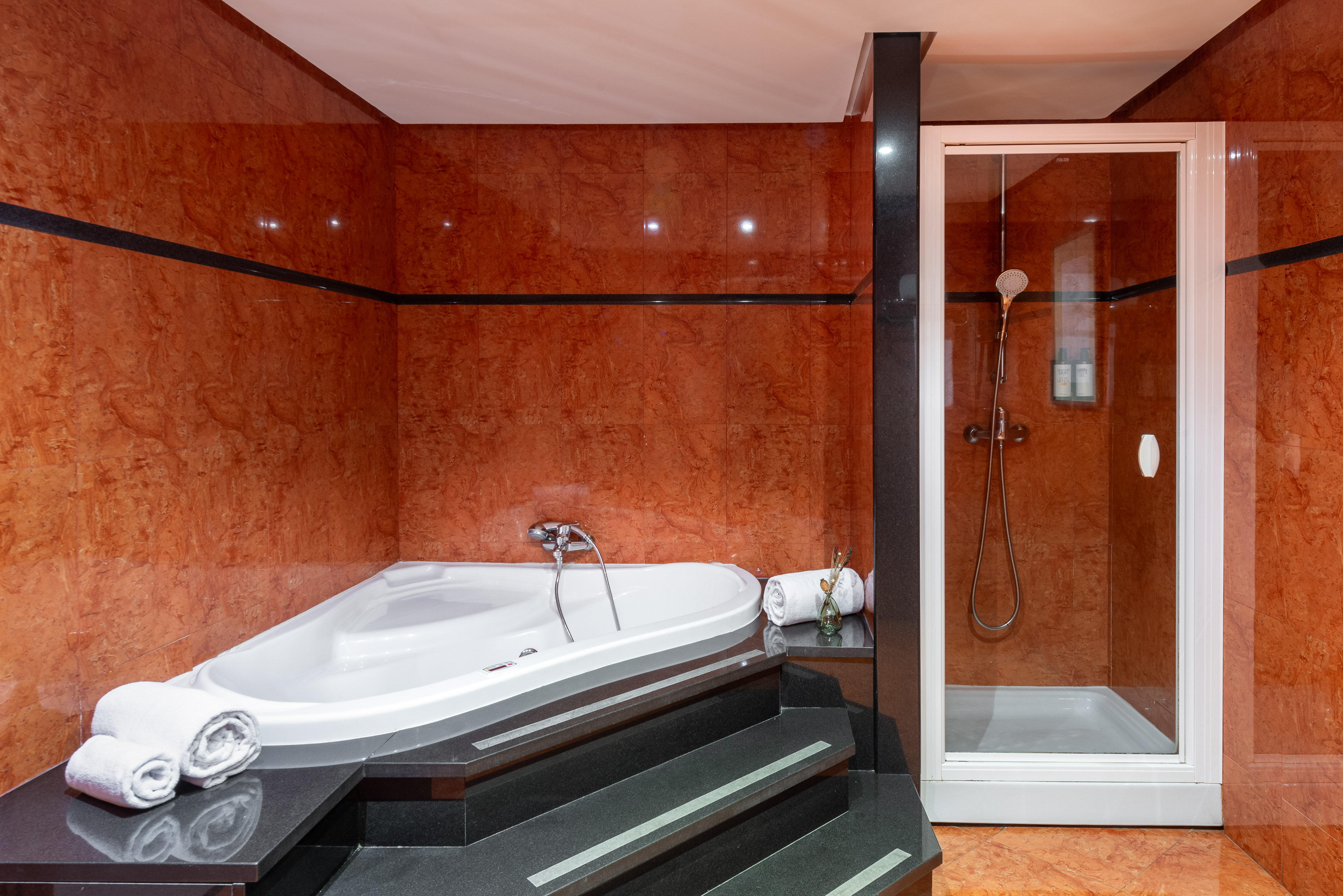 Luxury bathroom with a corner jacuzzi tub, glass shower, and red marble walls.