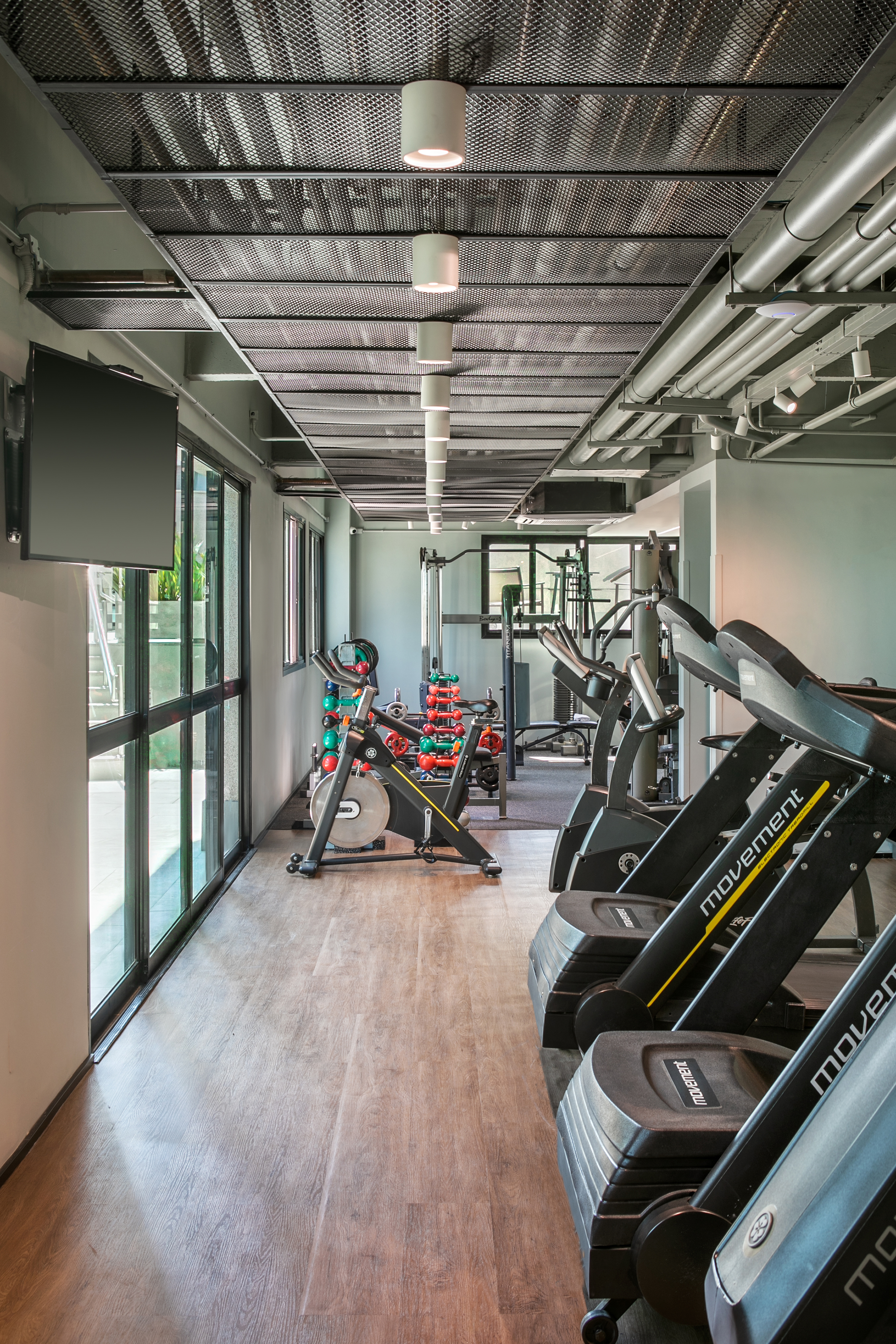 Bright, modern gym with treadmills, exercise bike, dumbbells, and wooden floor.