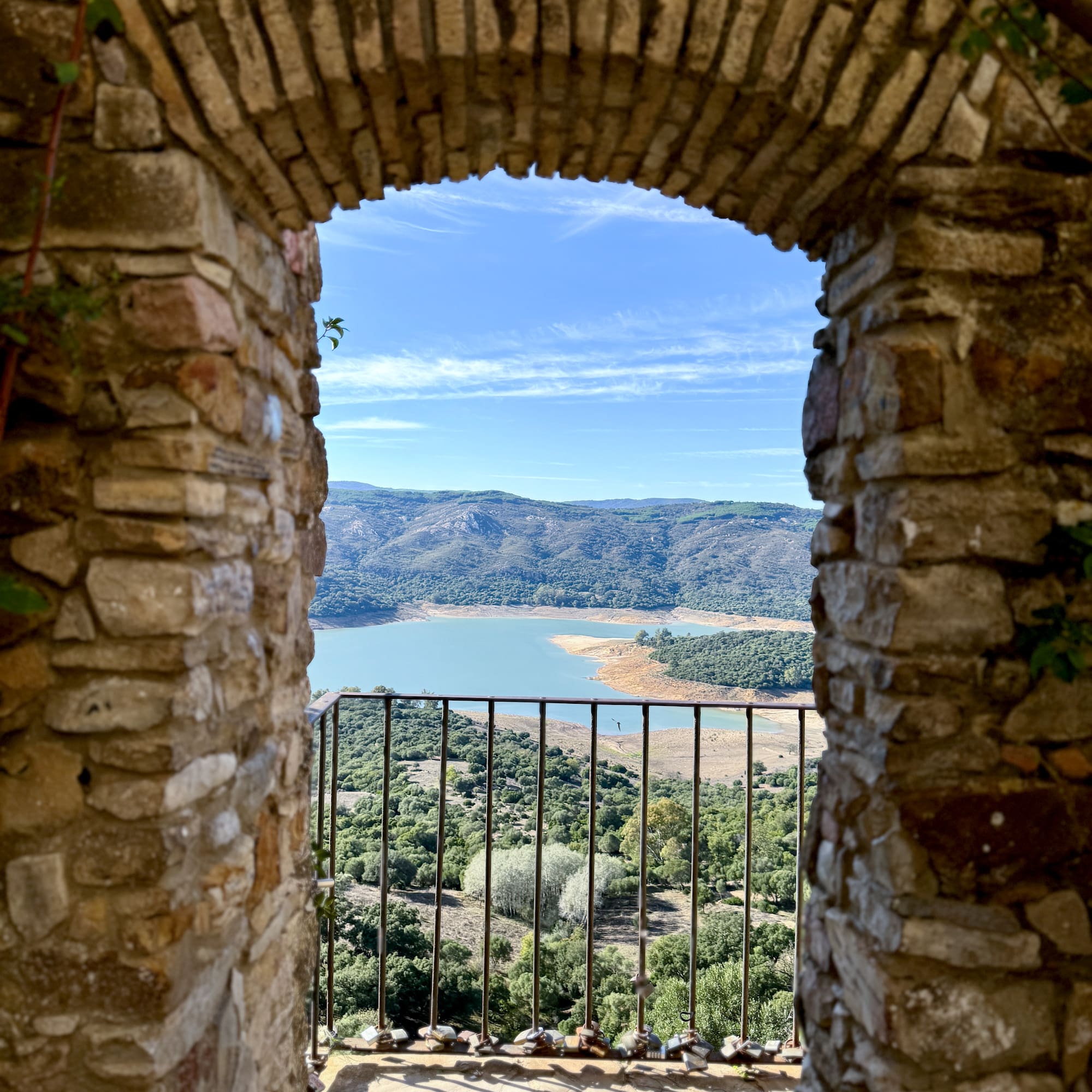 Historic stone archway framing a mountain lake view with love locks on railing.