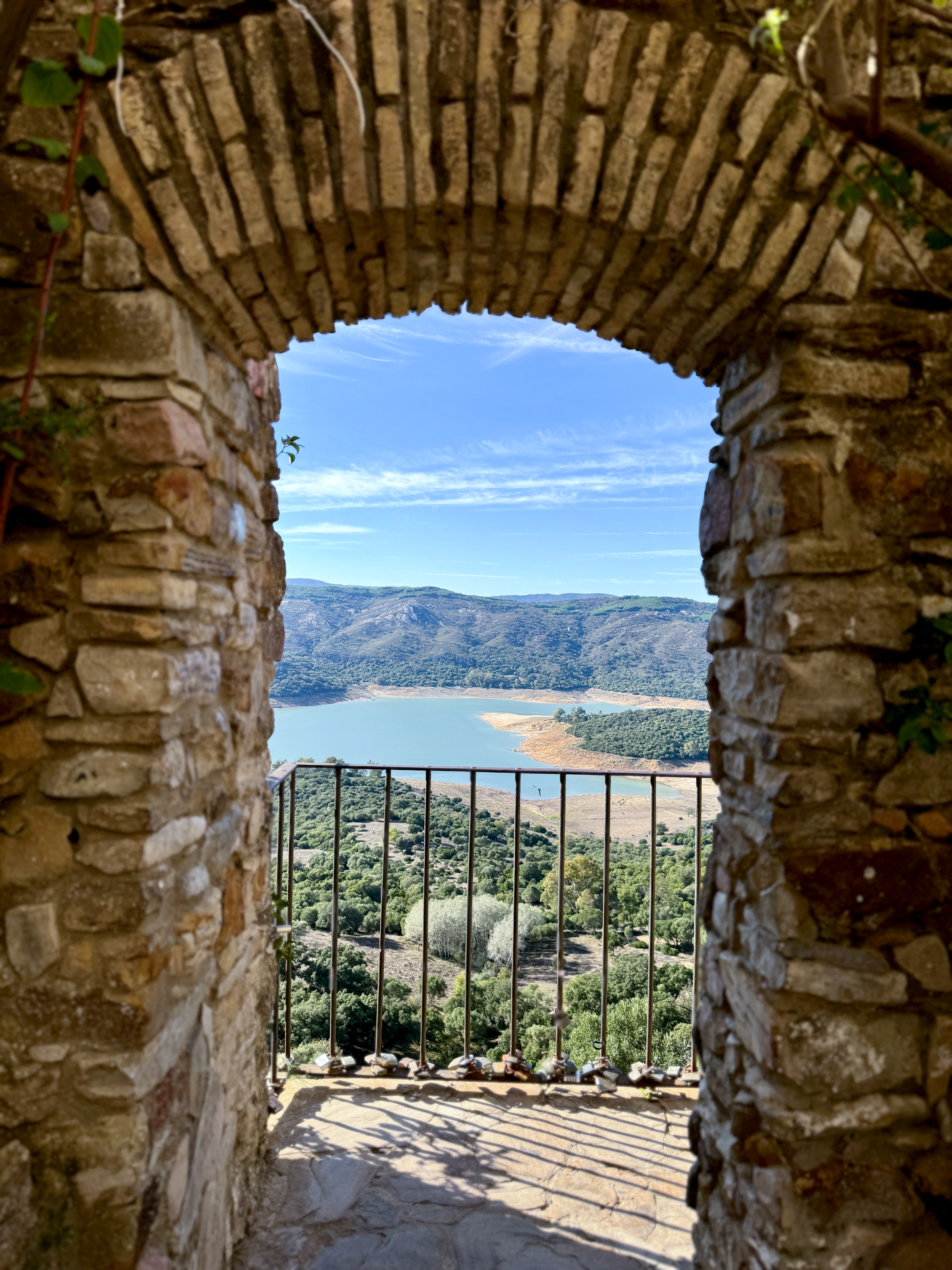 Historic stone archway framing a mountain lake view with love locks on railing.