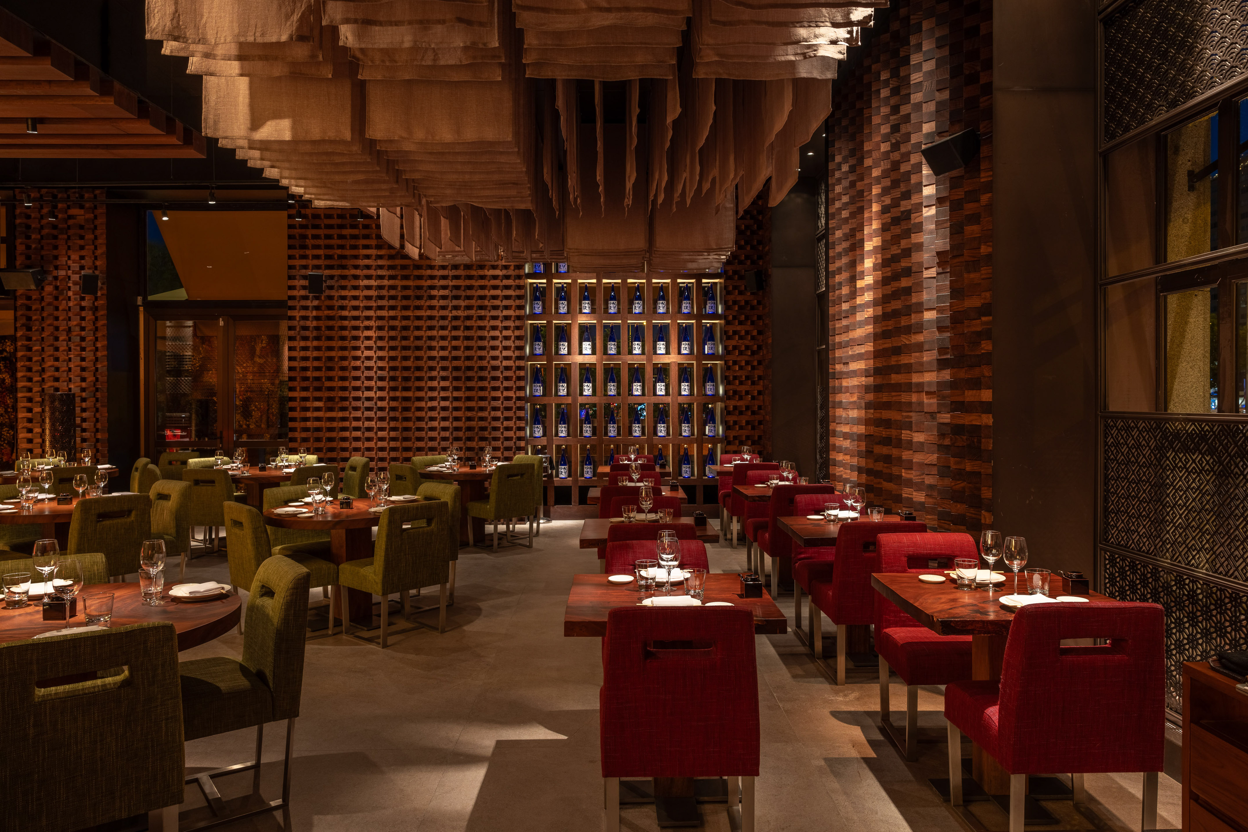 Upscale restaurant dining room with wood tables, red/green chairs, and sake wall.