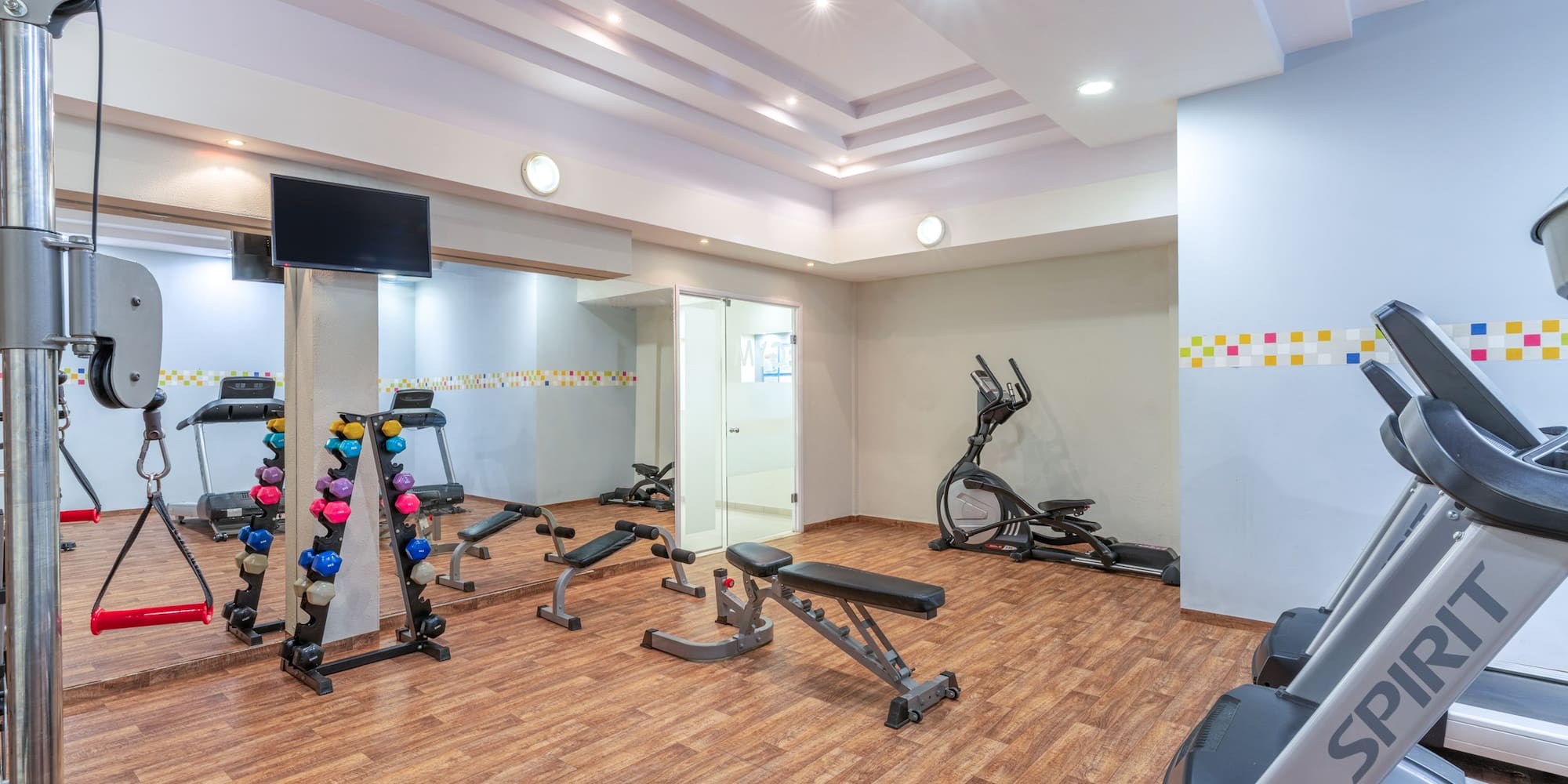 Bright gymnasium featuring treadmills, dumbbells, elliptical, and strength training equipment.