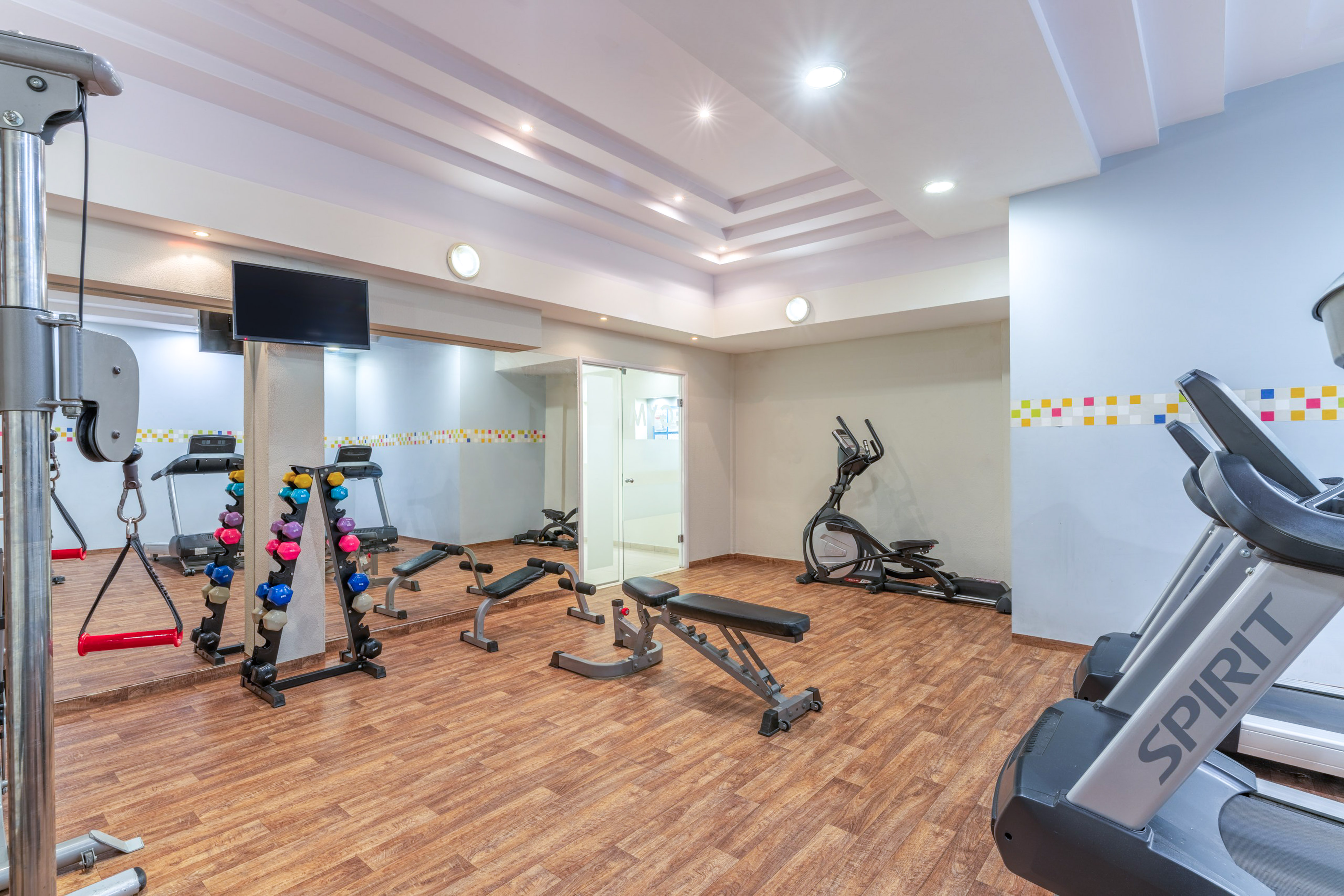 Bright gymnasium featuring treadmills, dumbbells, elliptical, and strength training equipment.