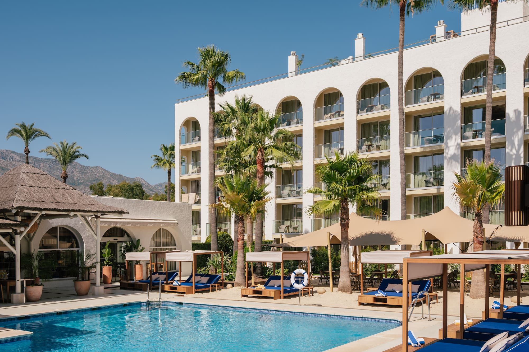 White resort hotel pool, palm trees, and mountain backdrop.