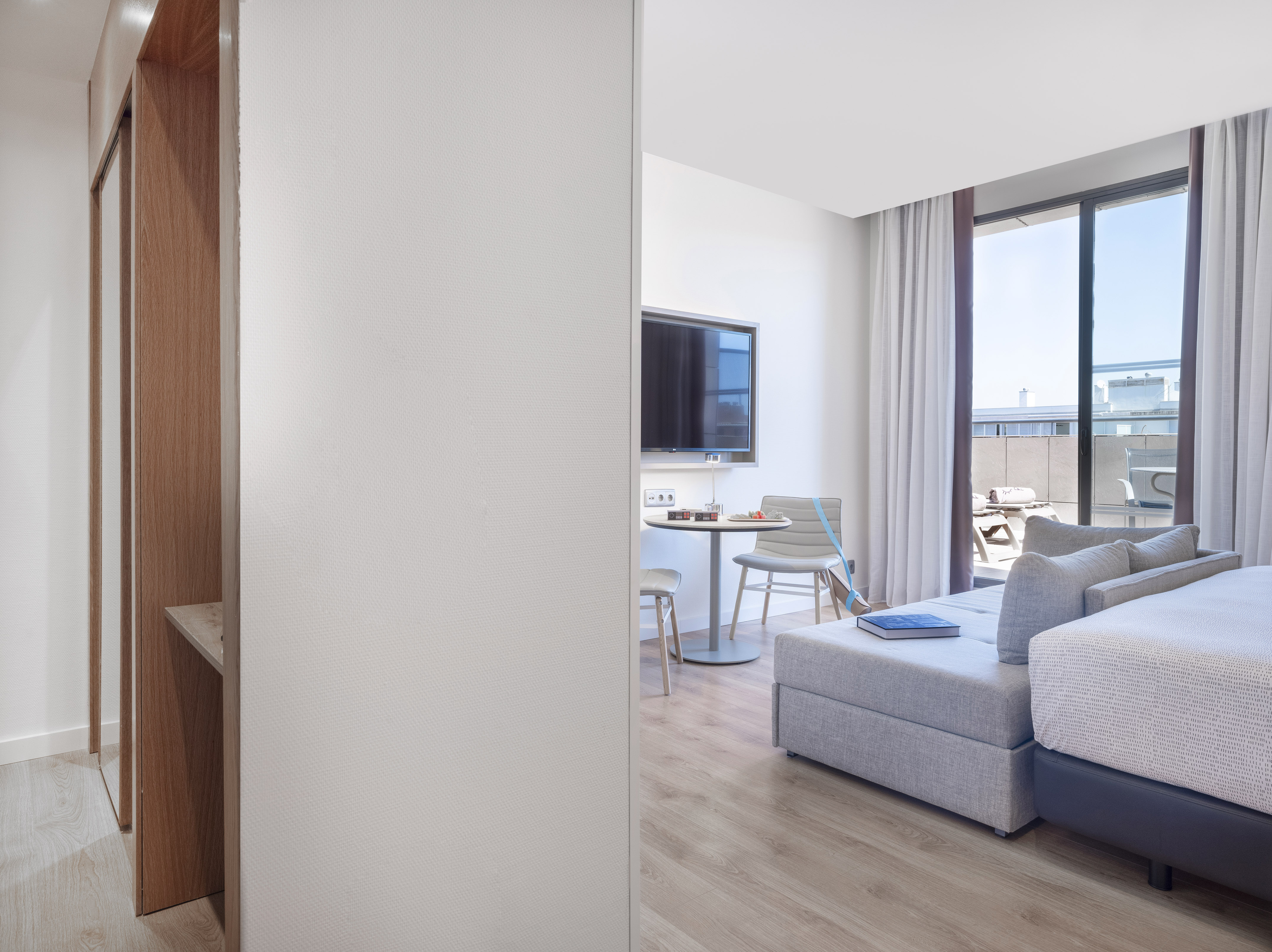 Modern studio apartment with grey sofa, TV, dining table, and balcony.