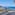Panoramic balcony view of a sunny coastal town, blue ocean, and rugged cliffs.
