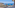 Panoramic balcony view of a sunny coastal town, blue ocean, and rugged cliffs.