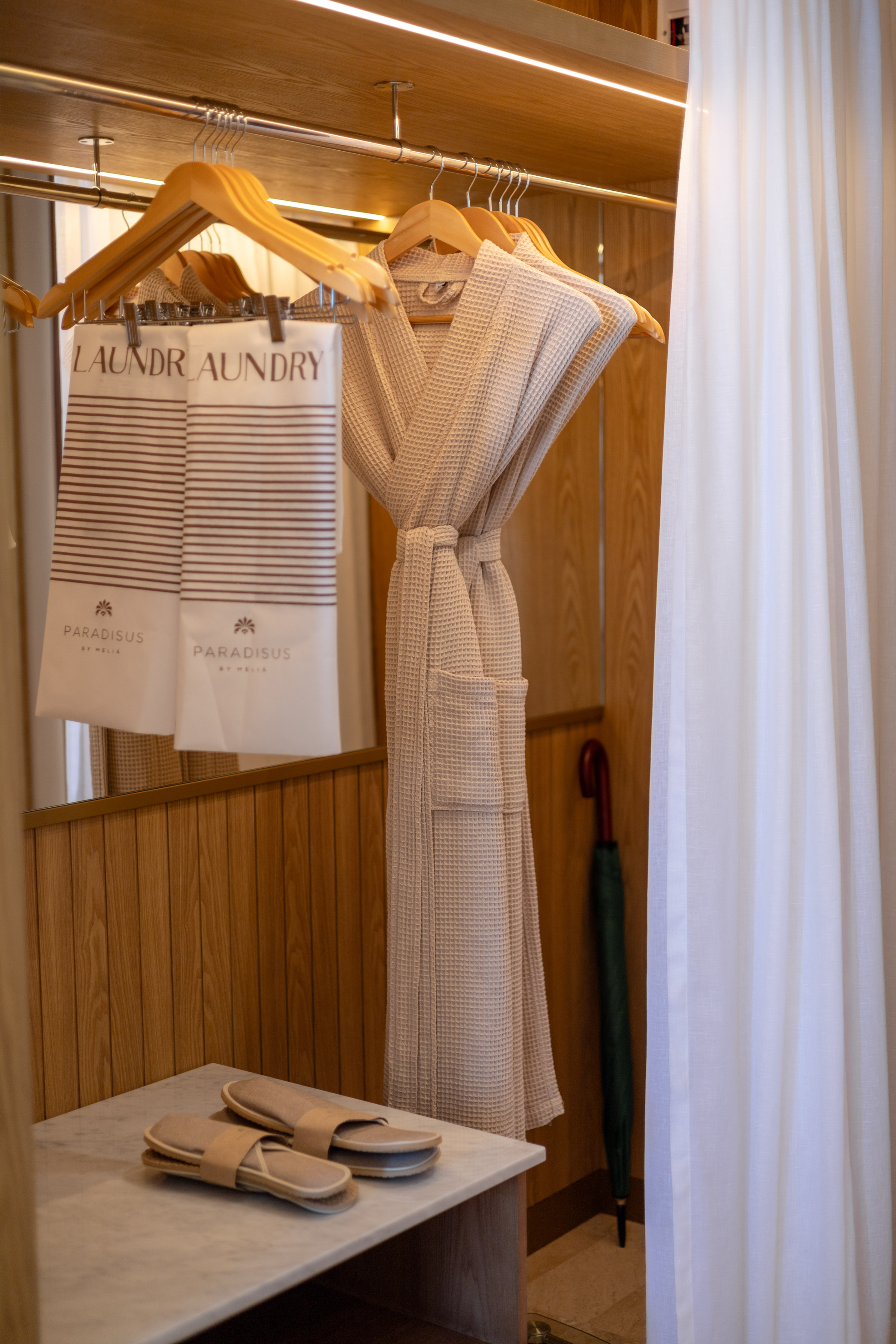 Guest room closet with beige waffle bathrobe, Paradissus laundry bags, and slippers.