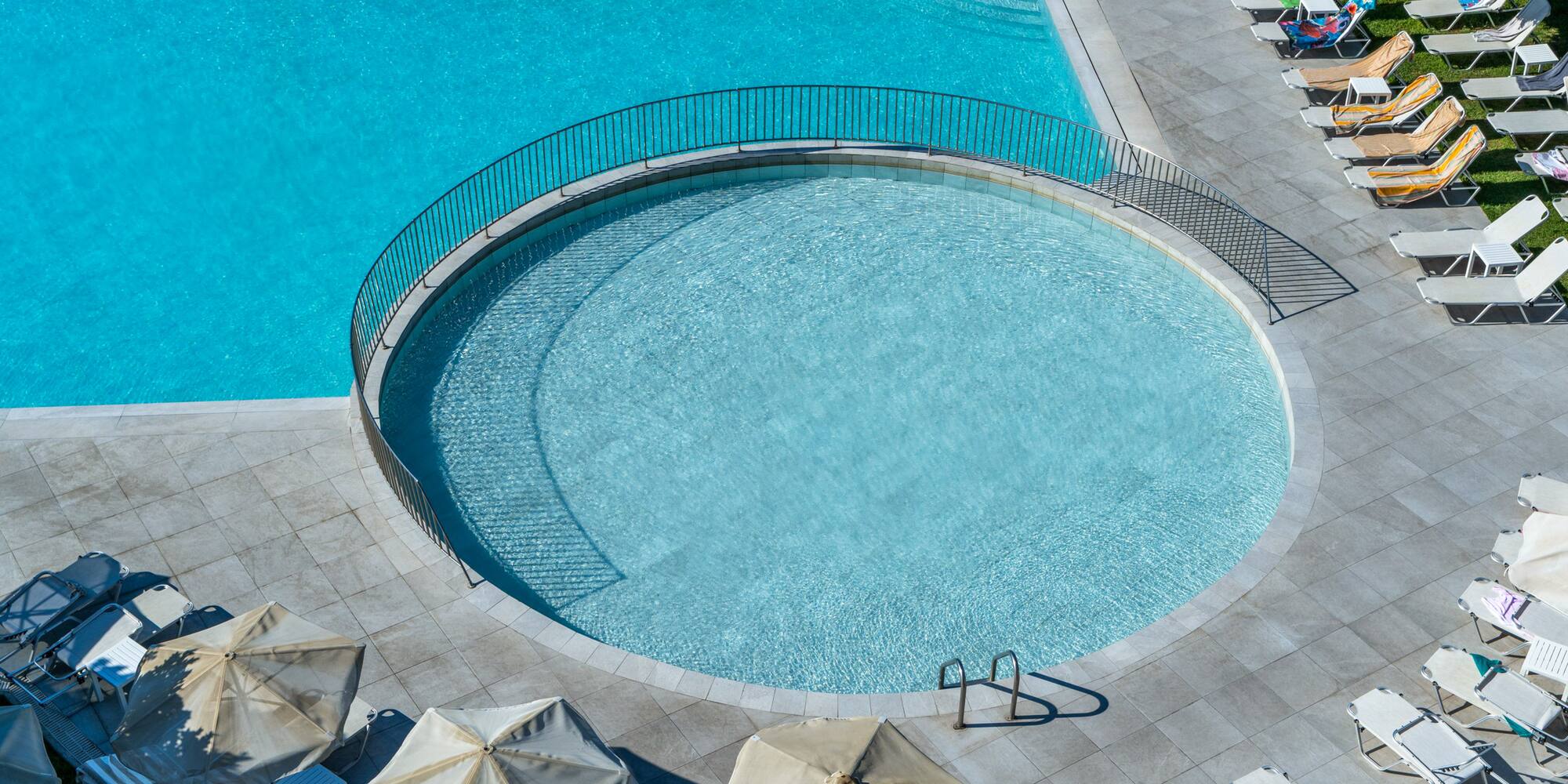 Blue resort swimming pool with circular pool, lounge chairs, and umbrellas.