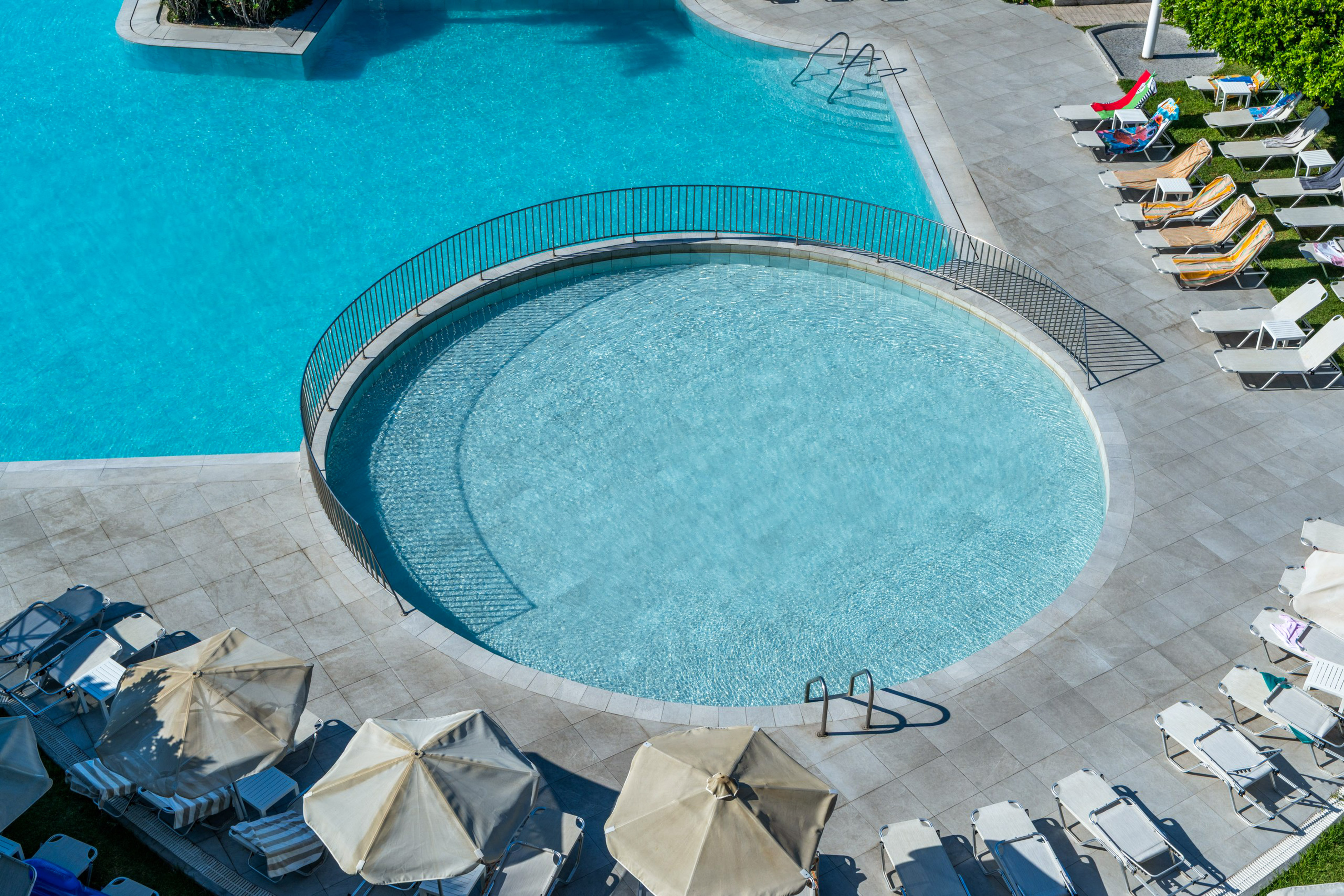 Blue resort swimming pool with circular pool, lounge chairs, and umbrellas.