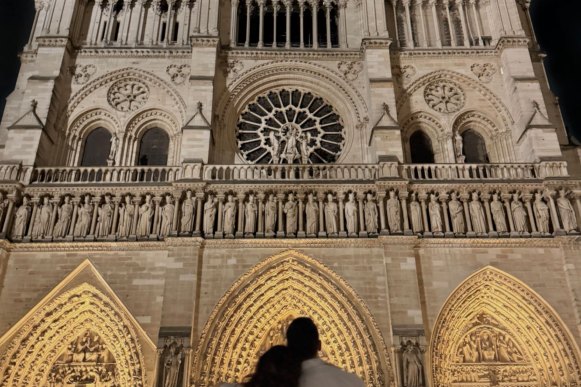 Couple viewing illuminated Notre Dame Cathedral Paris at night.