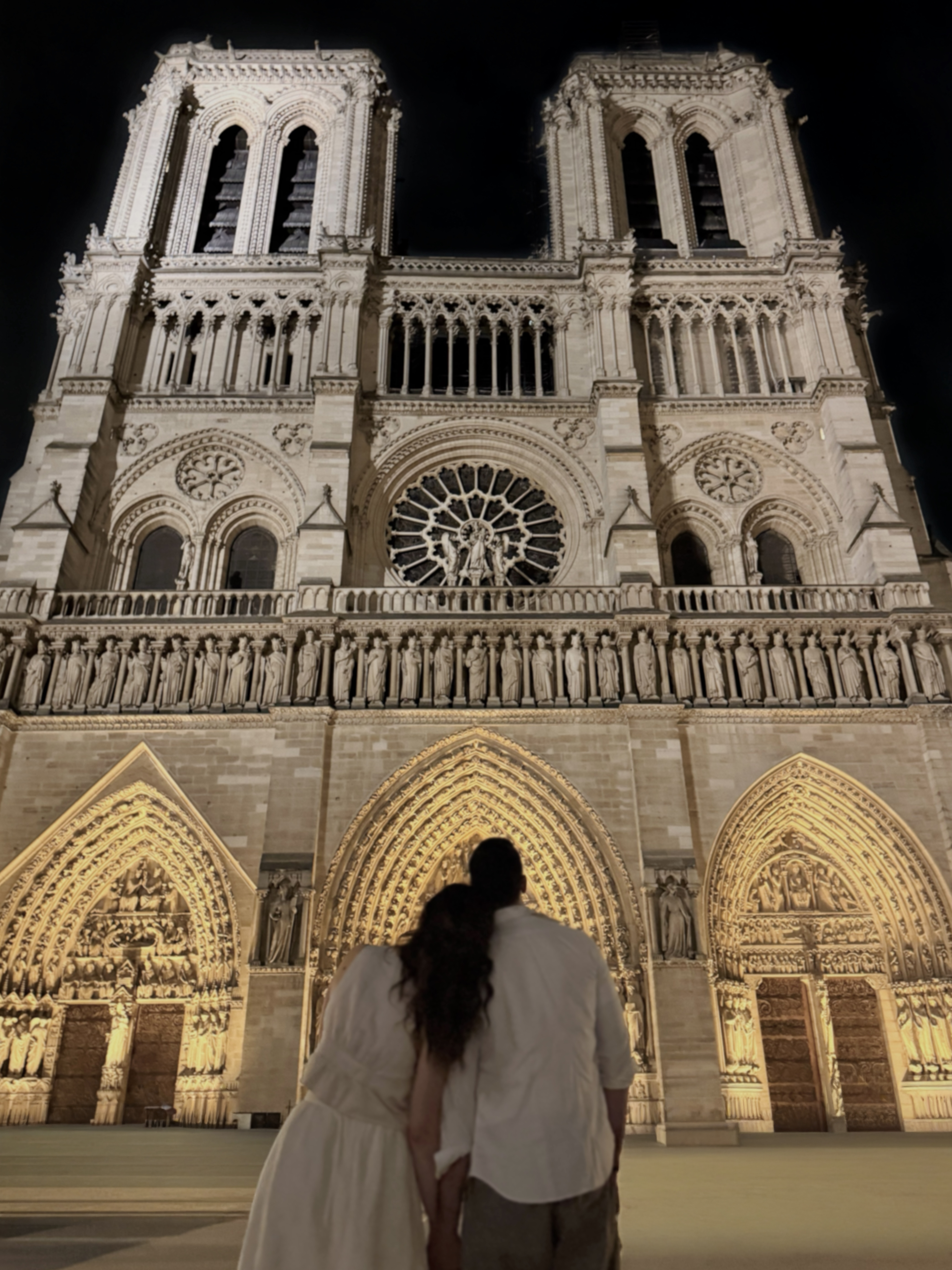 Couple viewing illuminated Notre Dame Cathedral Paris at night.