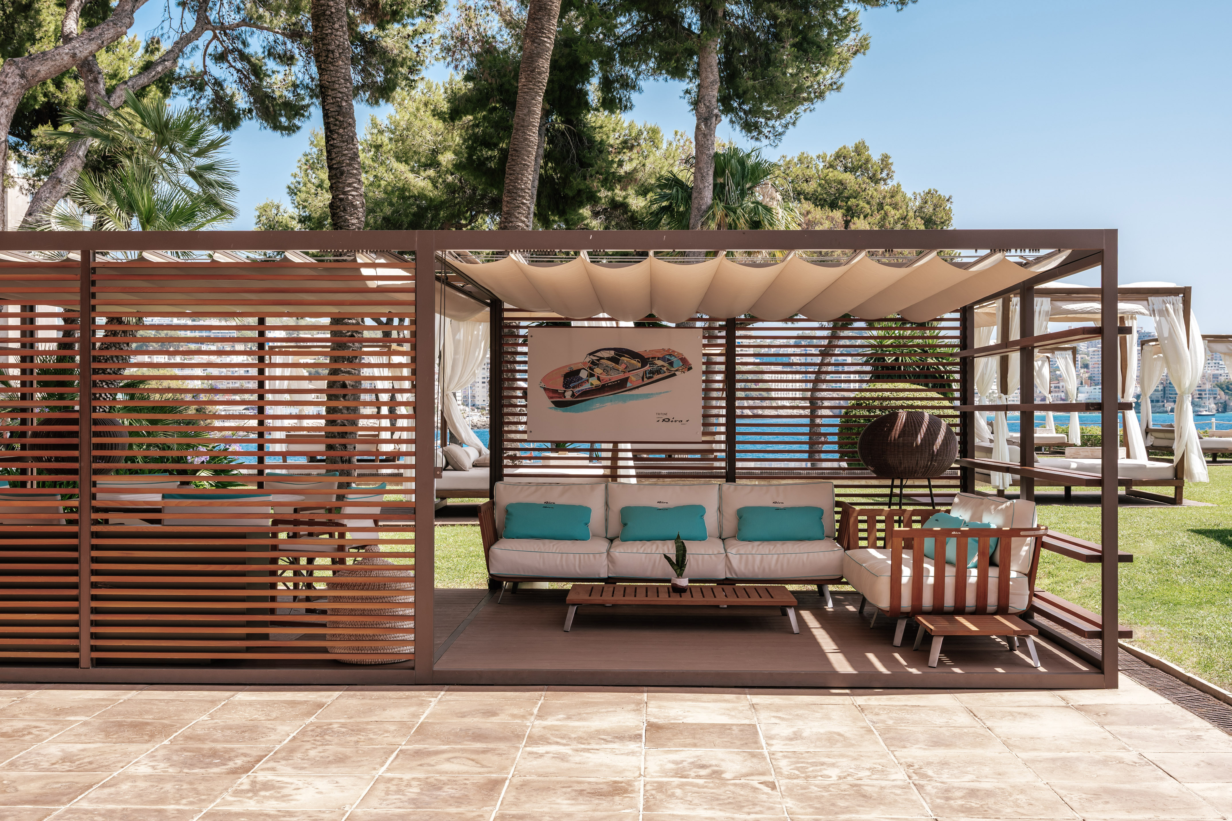 Outdoor pergola lounge with white sofa, blue cushions, ocean view.