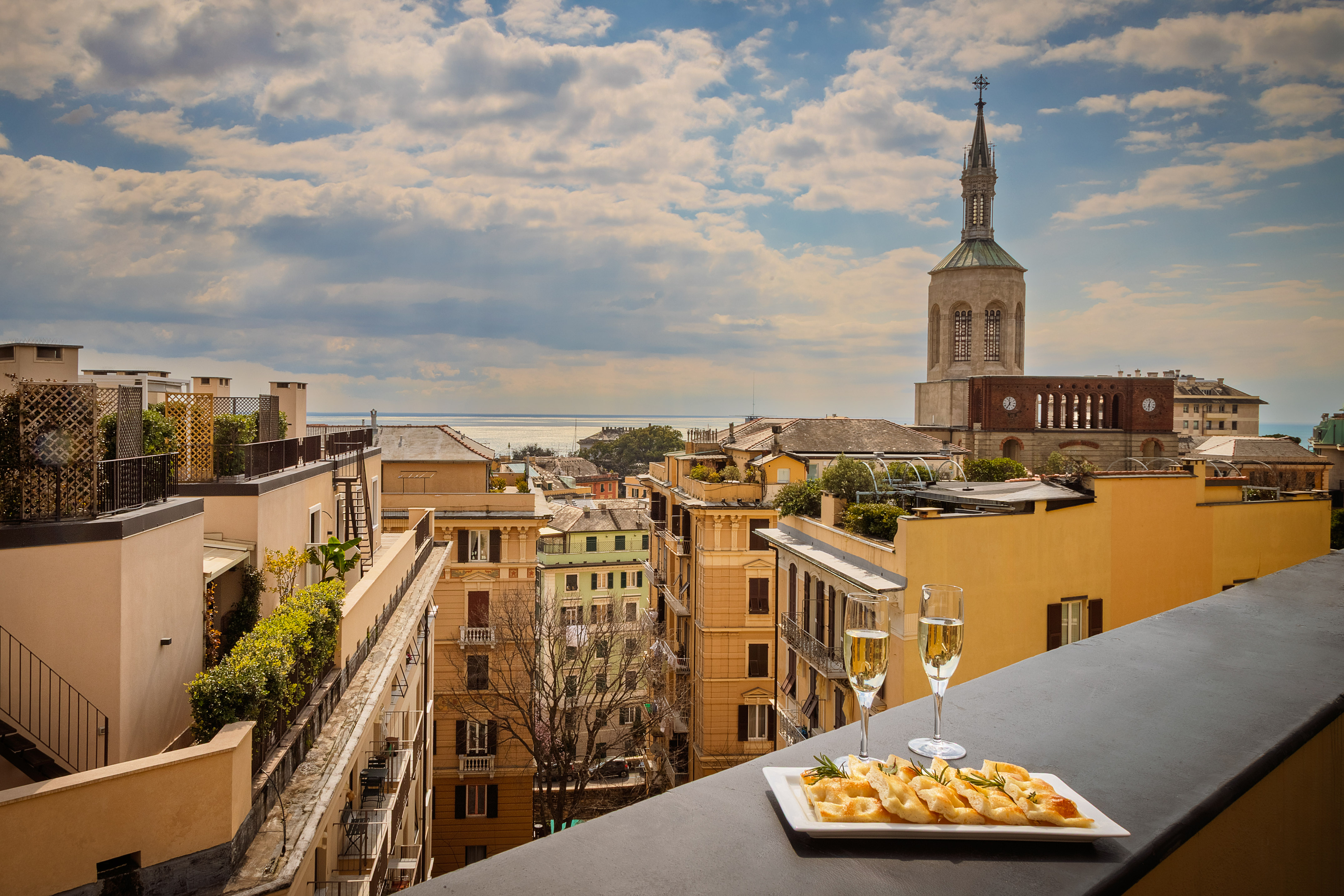 Balcony view: historic Italian city, sparkling sea, church, champagne, focaccia.