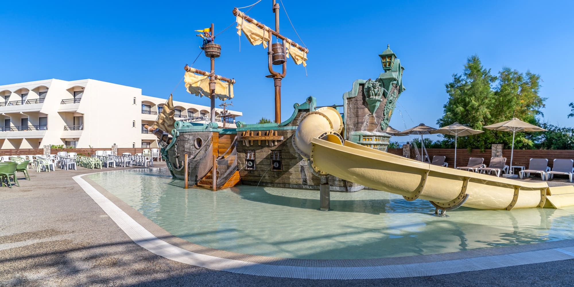 Pirate ship water playground with yellow slide at resort pool and hotel.