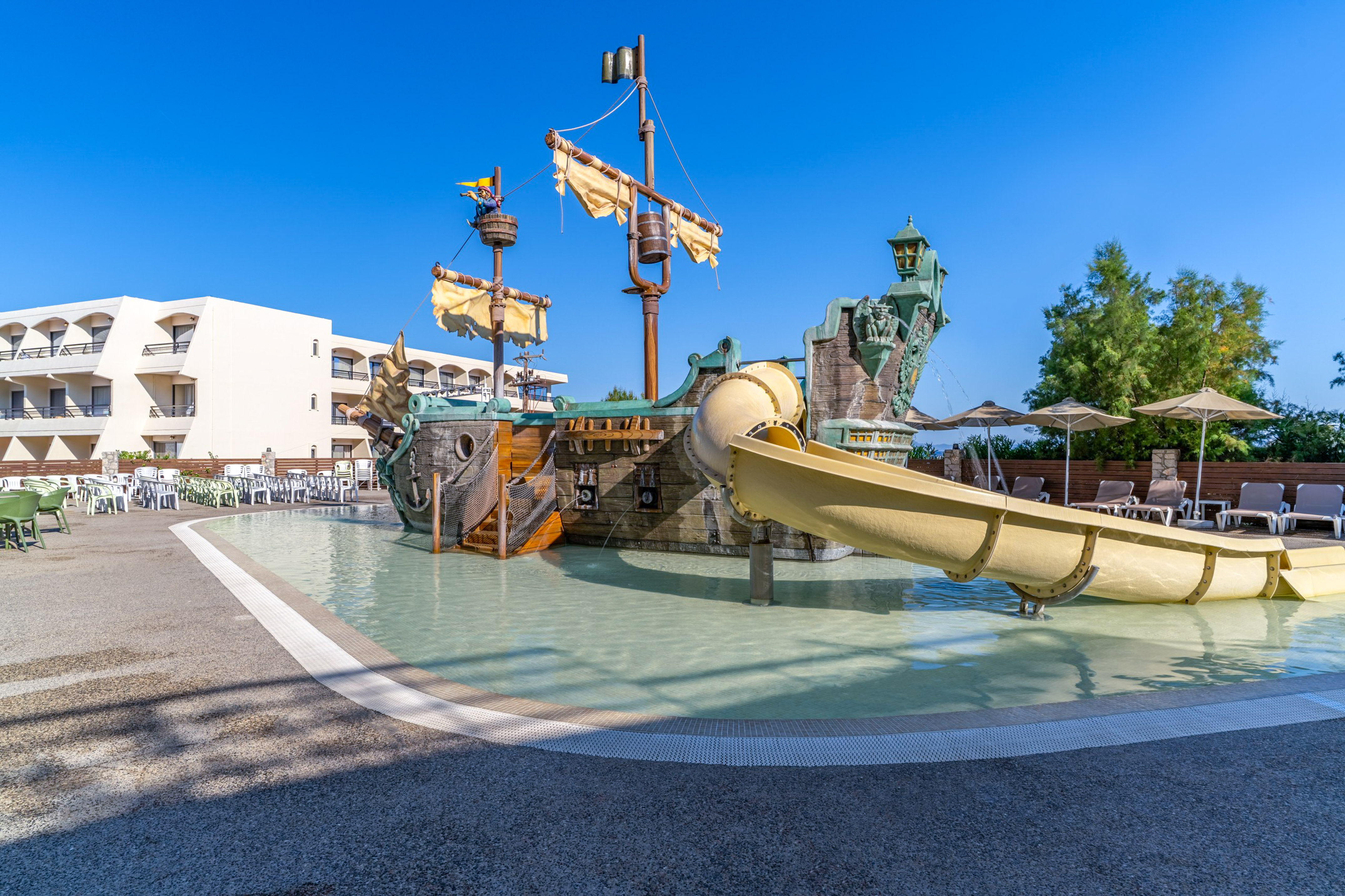 Pirate ship water playground with yellow slide at resort pool and hotel.