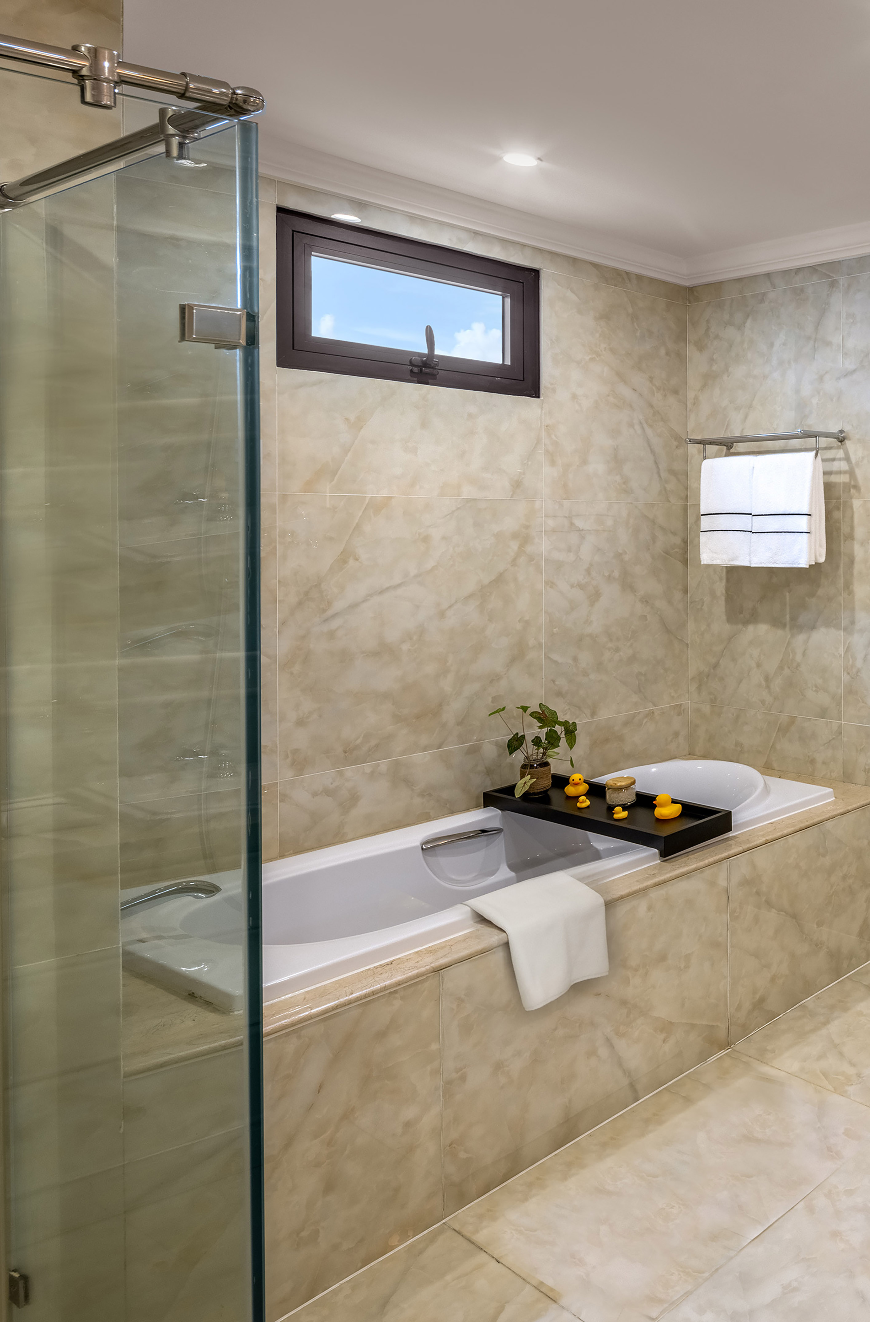 Modern tiled bathroom with bathtub, glass shower, and window.