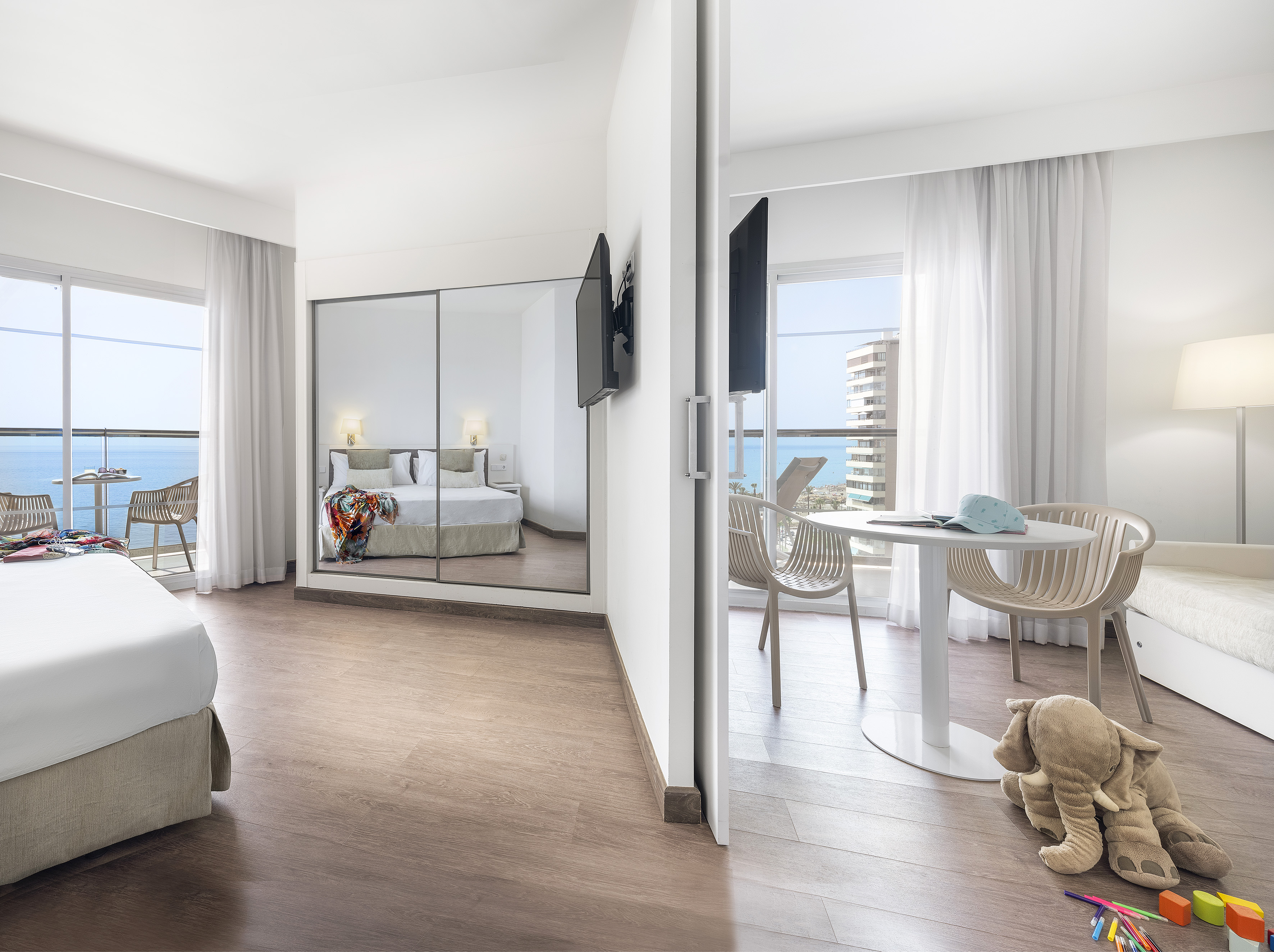 Modern hotel suite with sea view balcony, bedroom, and kid-friendly space.