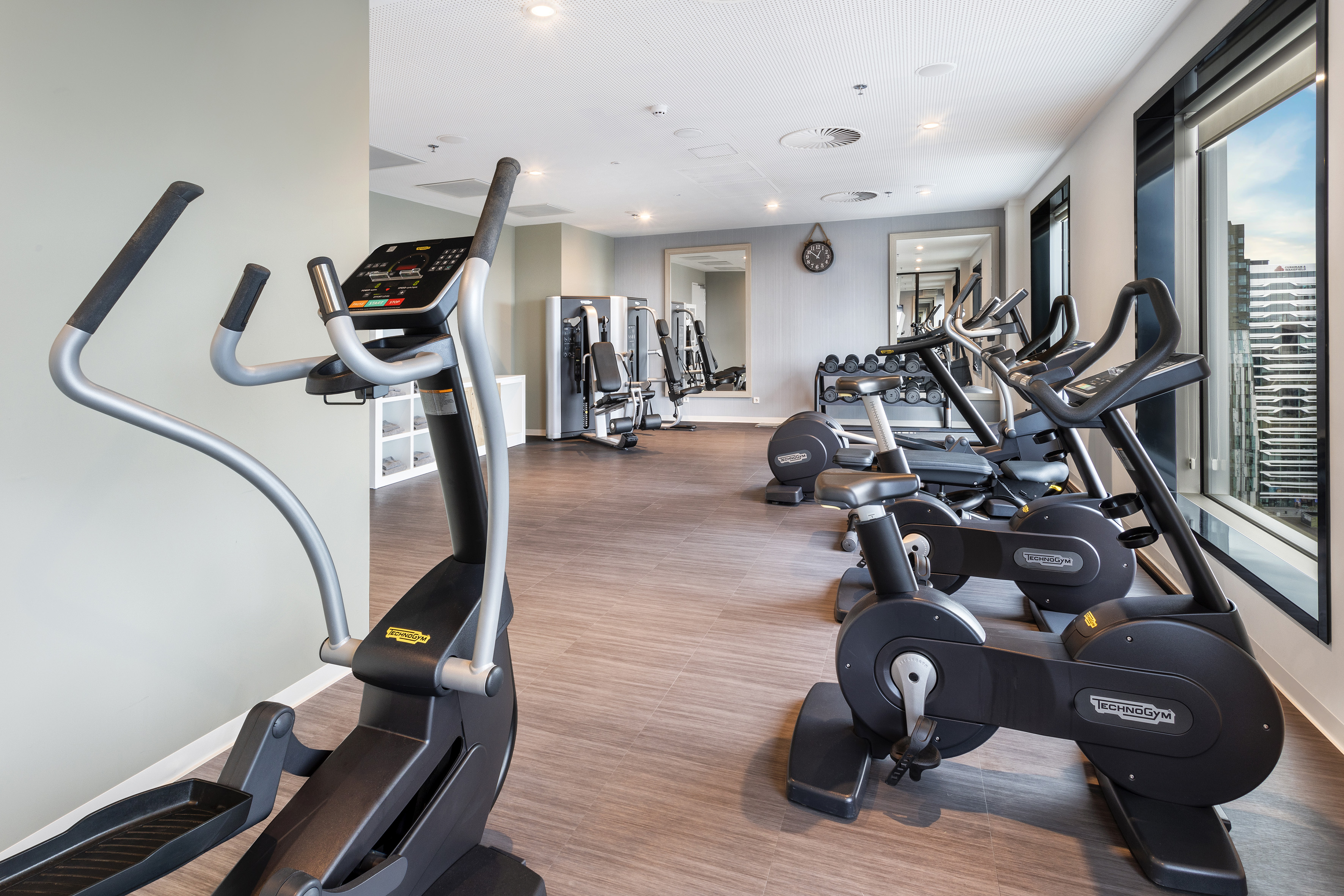 Well-equipped gym with elliptical, bikes, weights, and large windows.