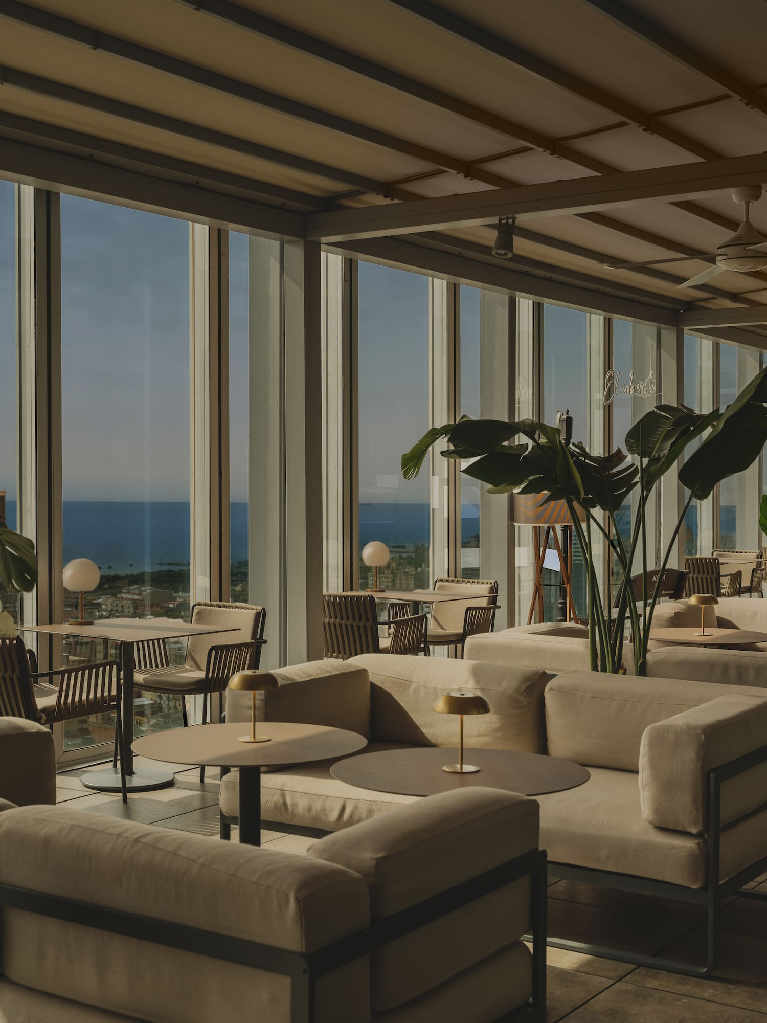 Rooftop lounge with ocean view, modern outdoor seating, and tropical plants.