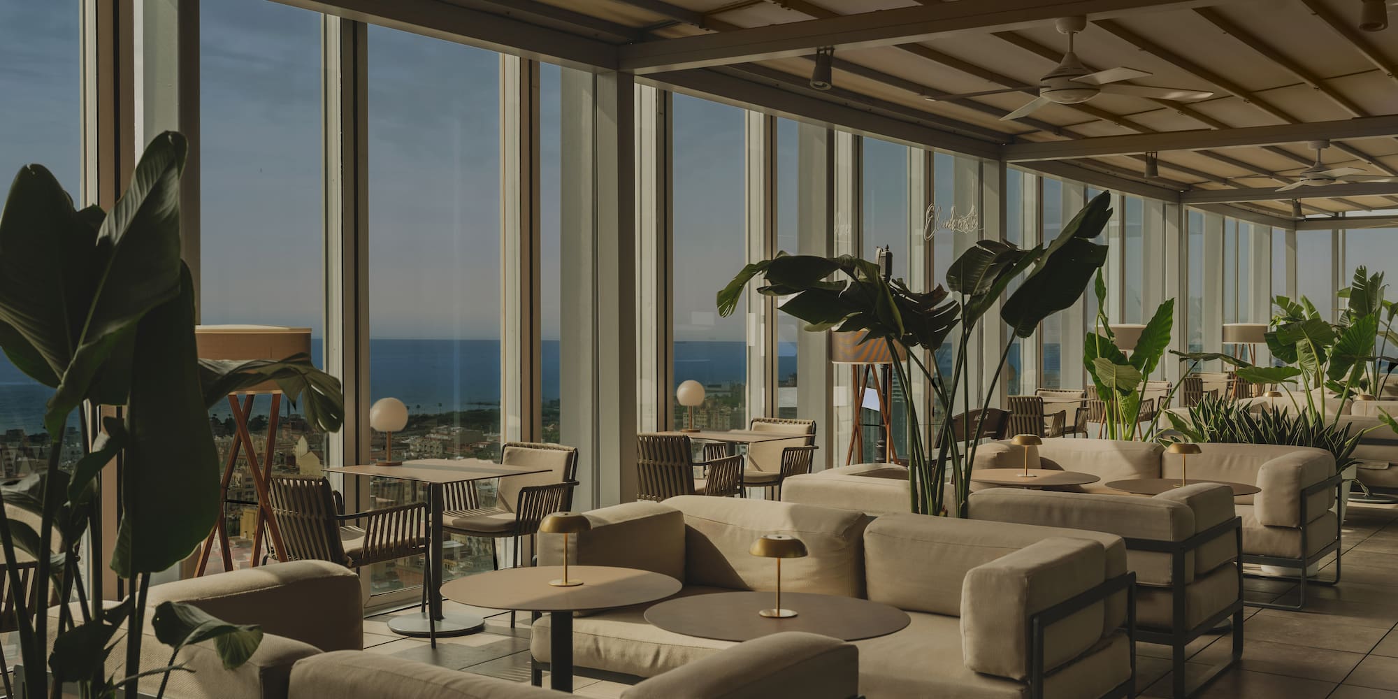 Rooftop lounge with ocean view, modern outdoor seating, and tropical plants.