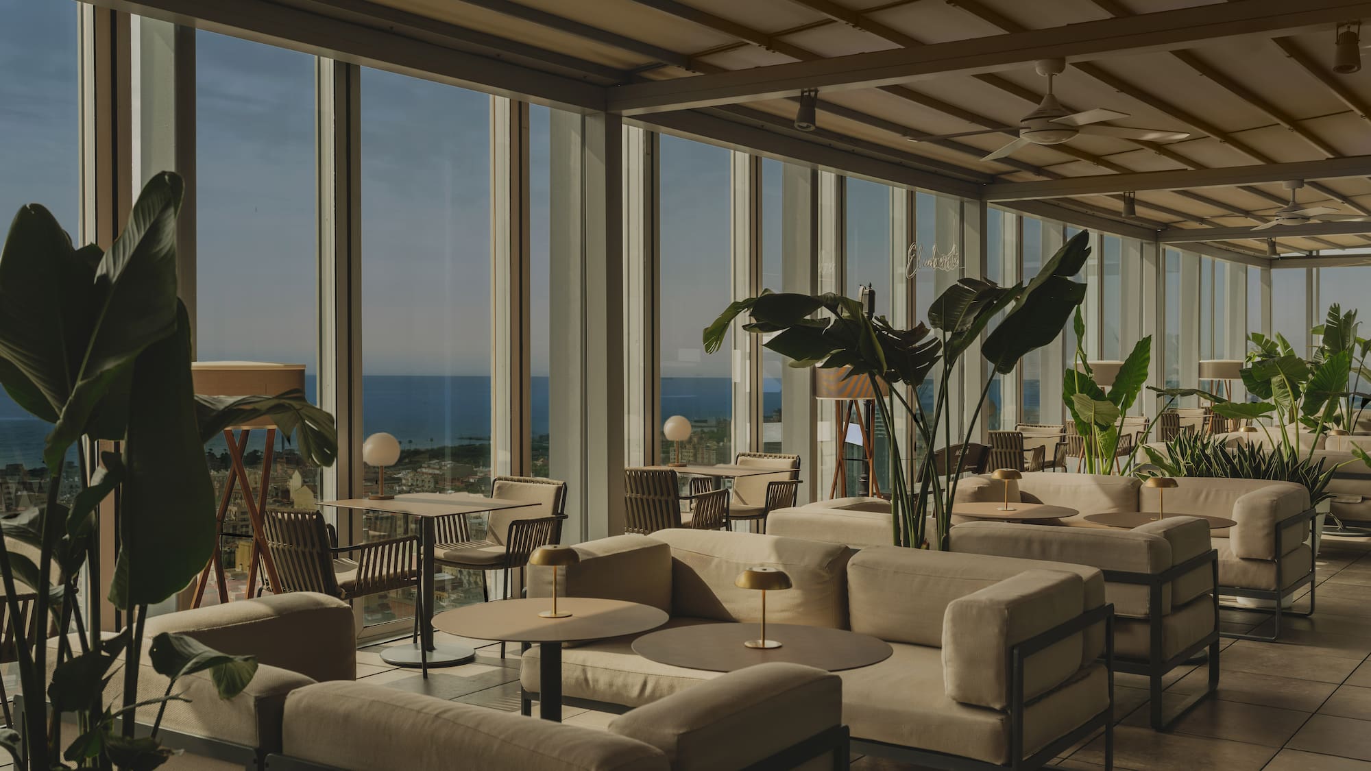 Rooftop lounge with ocean view, modern seating, and indoor plants.