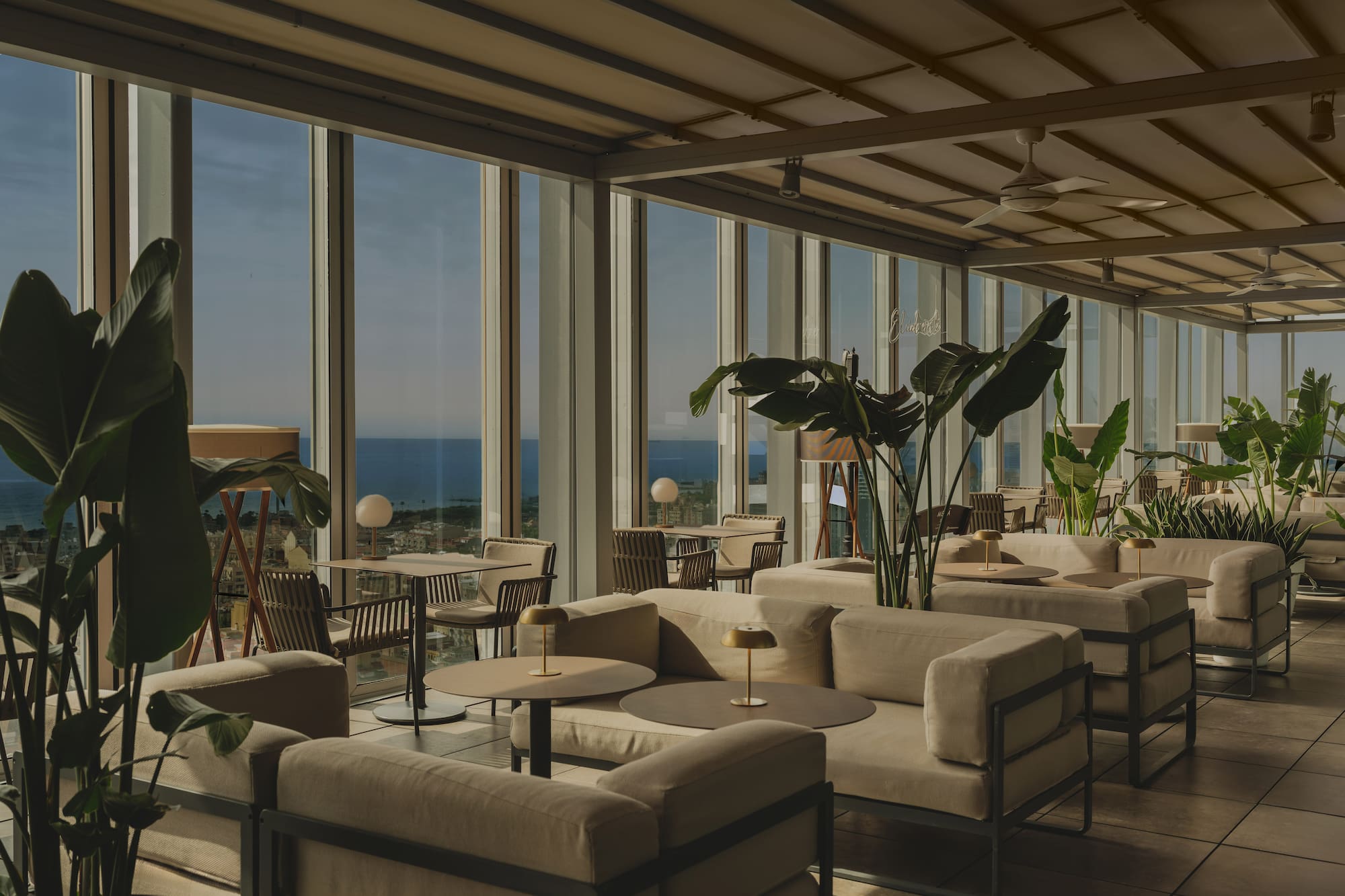 Rooftop lounge with ocean view, modern outdoor seating, and tropical plants.