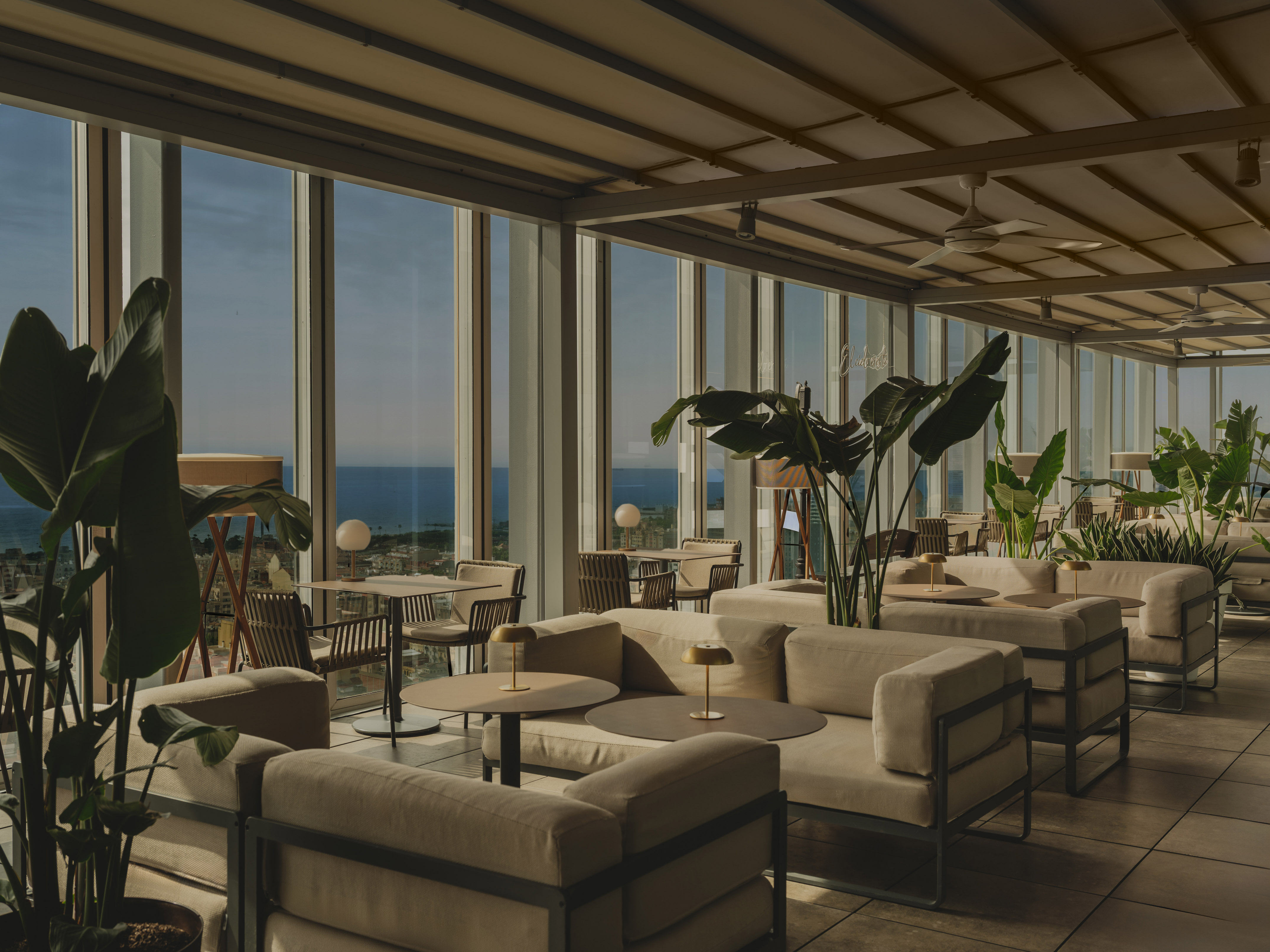 Rooftop lounge with ocean view, modern outdoor seating, and tropical plants.