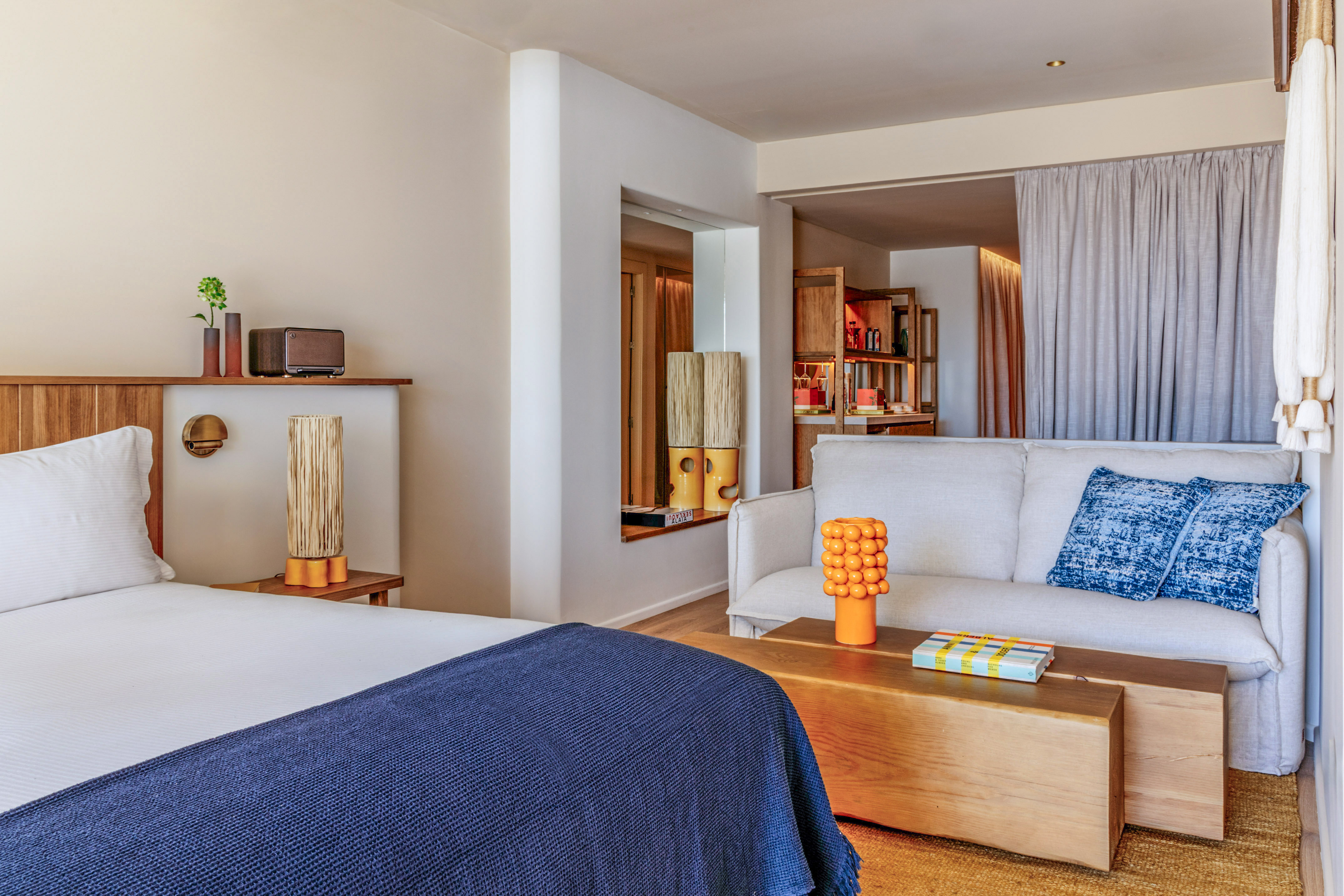 Modern hotel suite with bed, light sofa, blue accents, and wooden furniture.