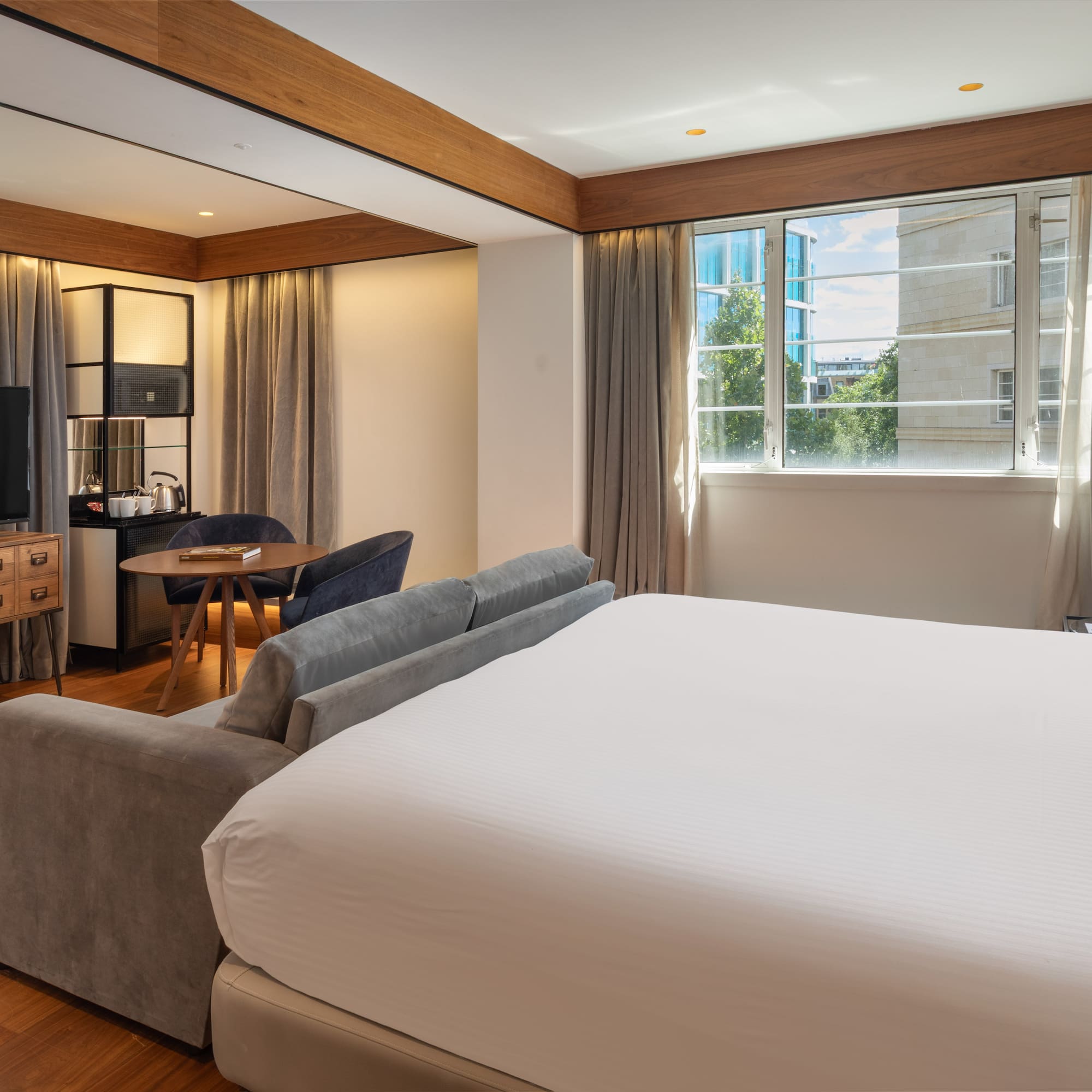 Modern hotel suite with king bed, sofa, workspace, and city view.