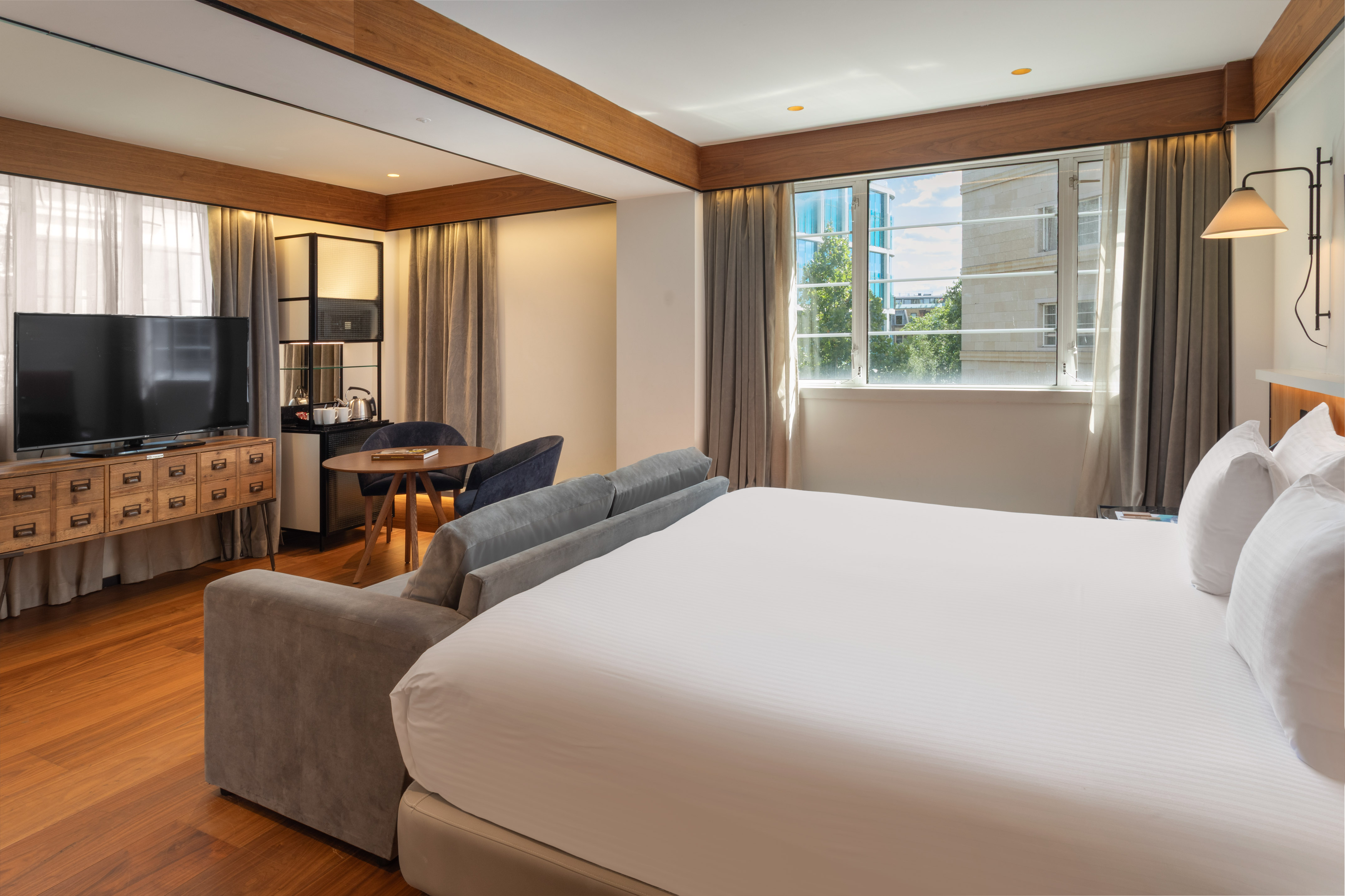 Modern hotel suite with king bed, sofa, workspace, and city view.