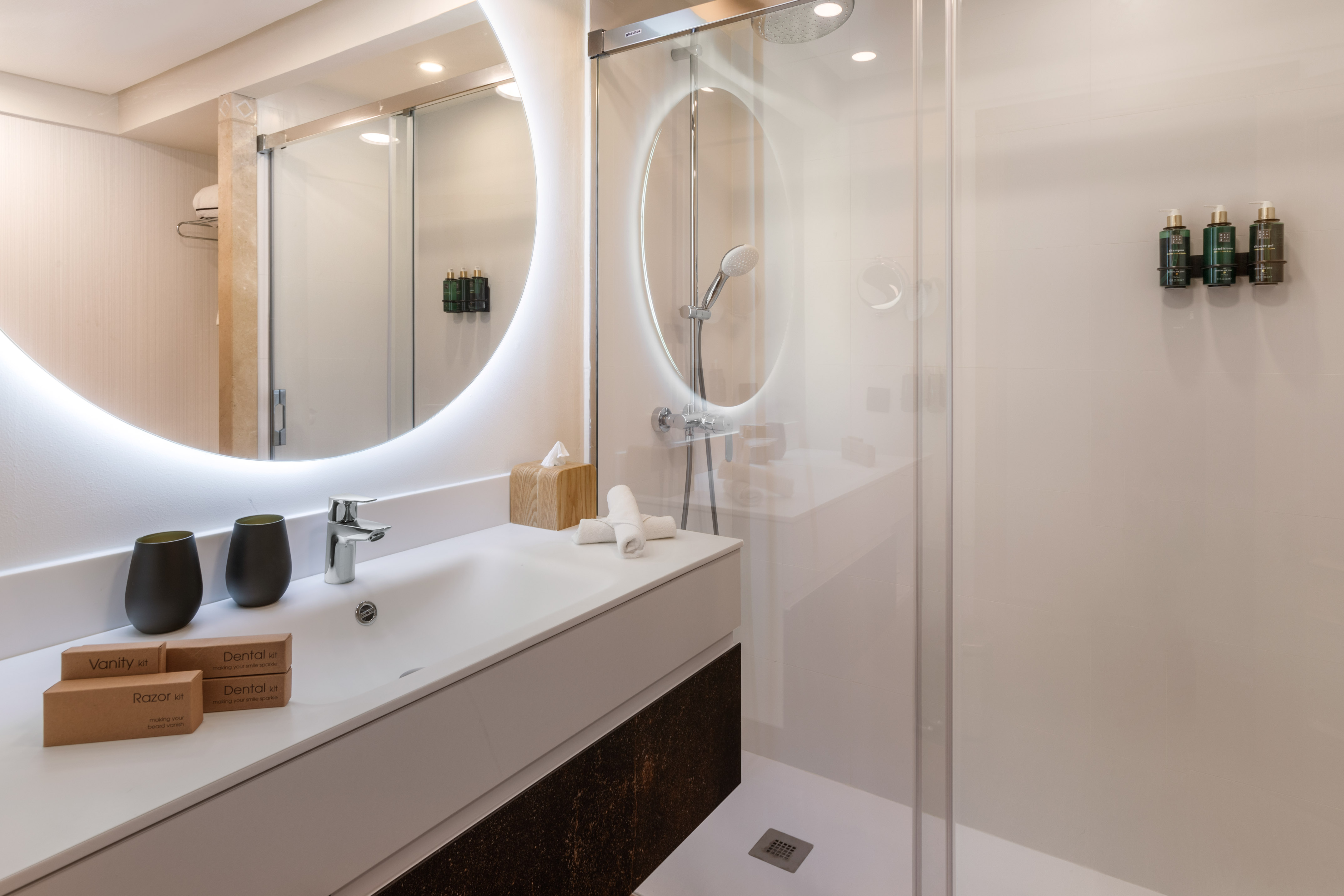 Modern bathroom with backlit mirror, vanity, shower, and hotel amenities.