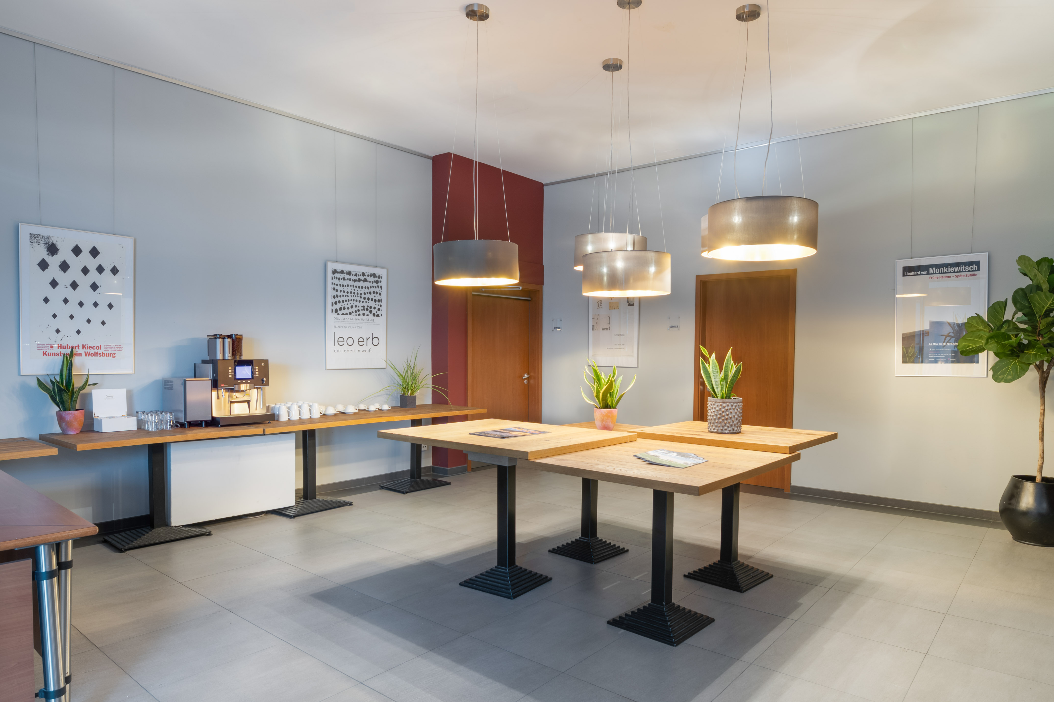 Modern office lobby with coffee station, art, wooden tables, and plants.