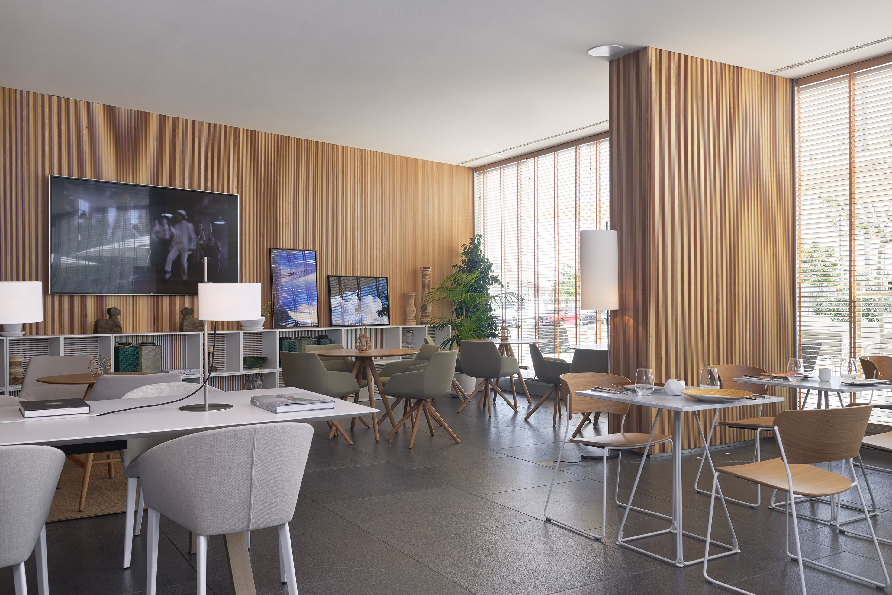 Modern cafe or lounge with wooden walls, diverse seating, TV, and large windows.