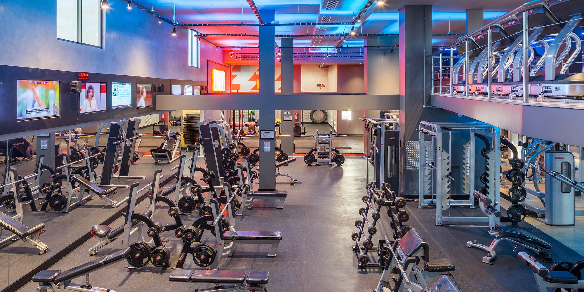 Modern gym with weights, cardio equipment, and vibrant blue and red lighting.