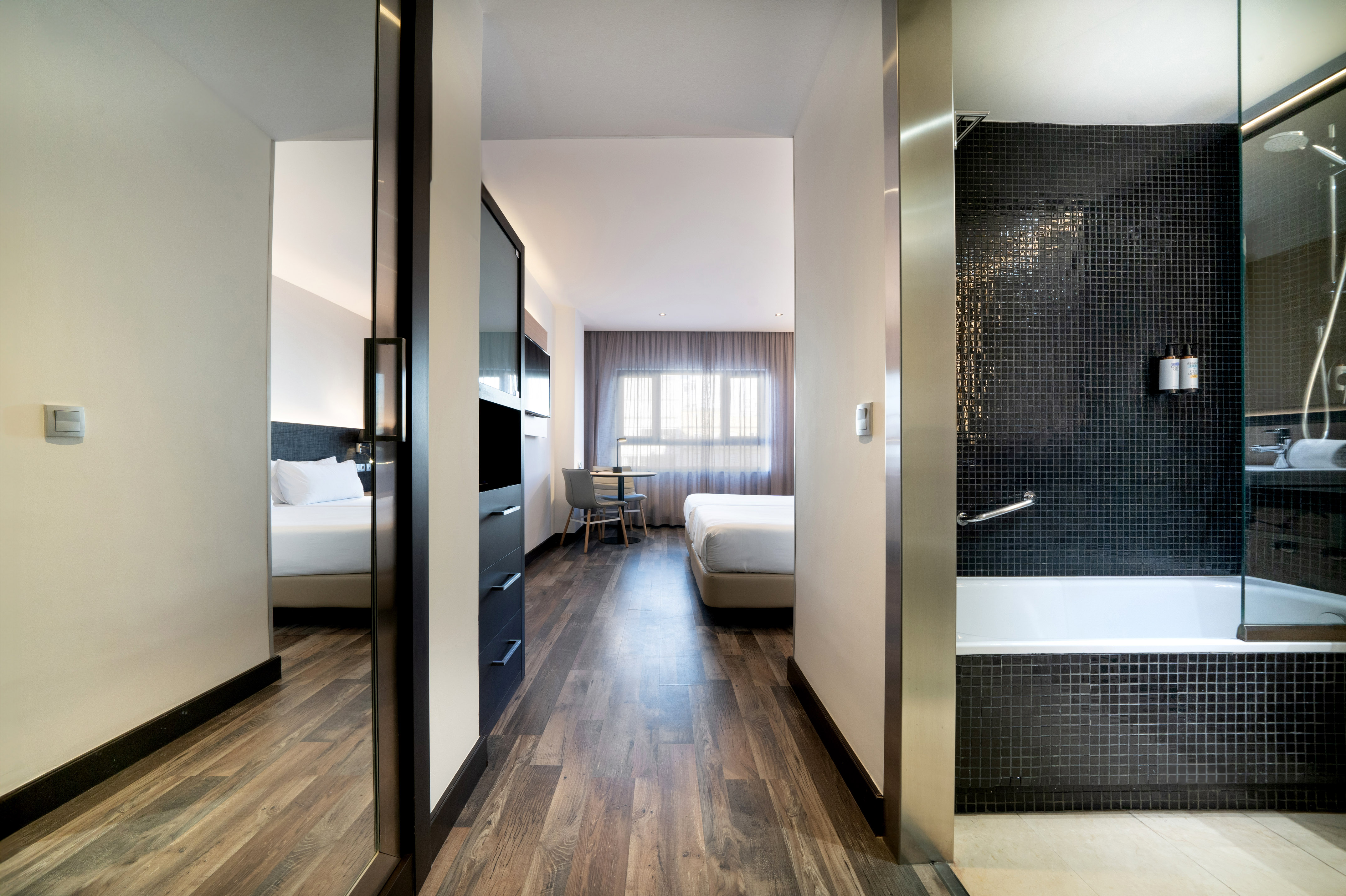 Modern hotel suite hallway to bedroom and black tiled bathroom.