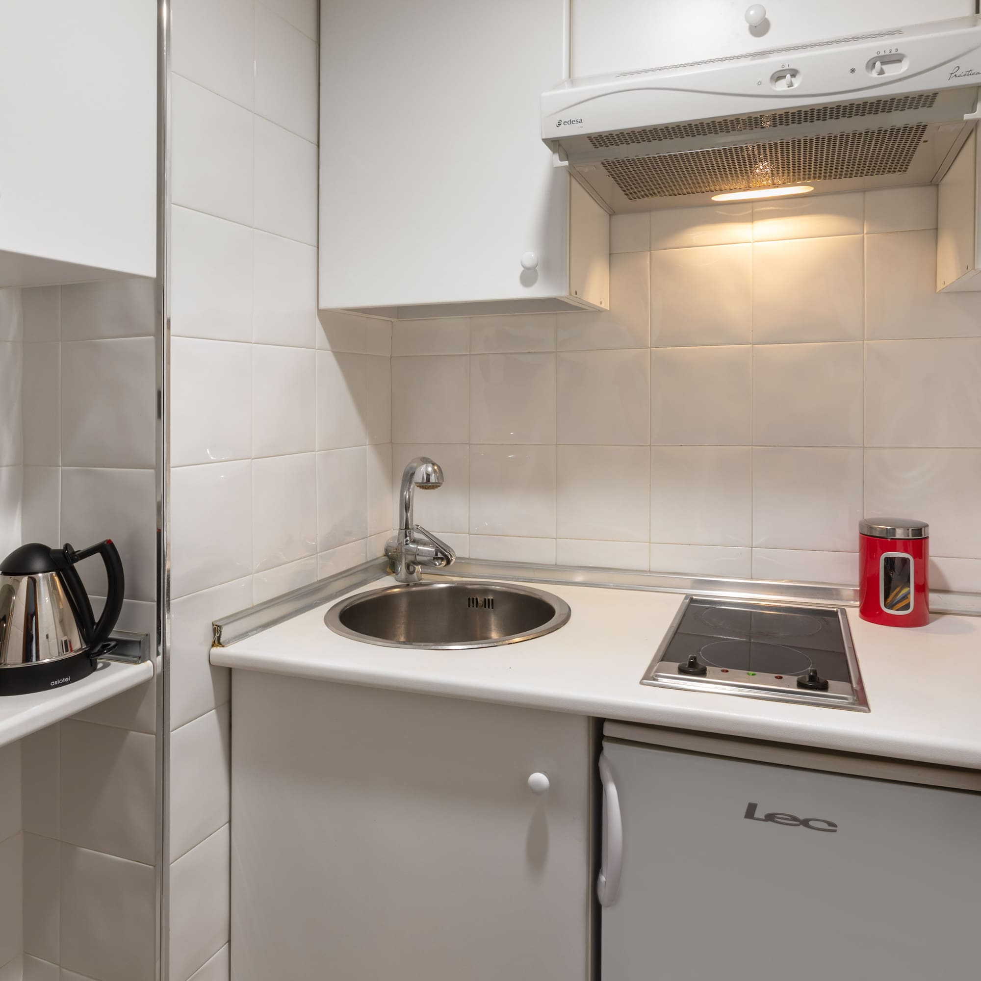 Compact white kitchenette with sink, stove, fridge, microwave, toaster, and kettle.