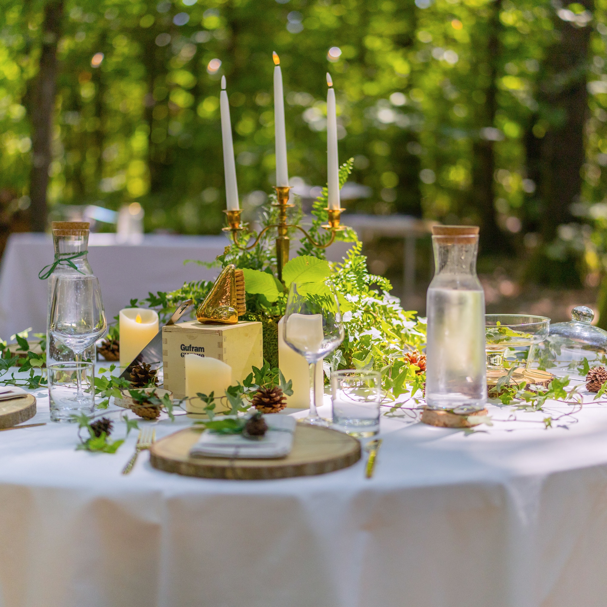 Rustic outdoor dining table with candelabra, greenery, candles in forest.