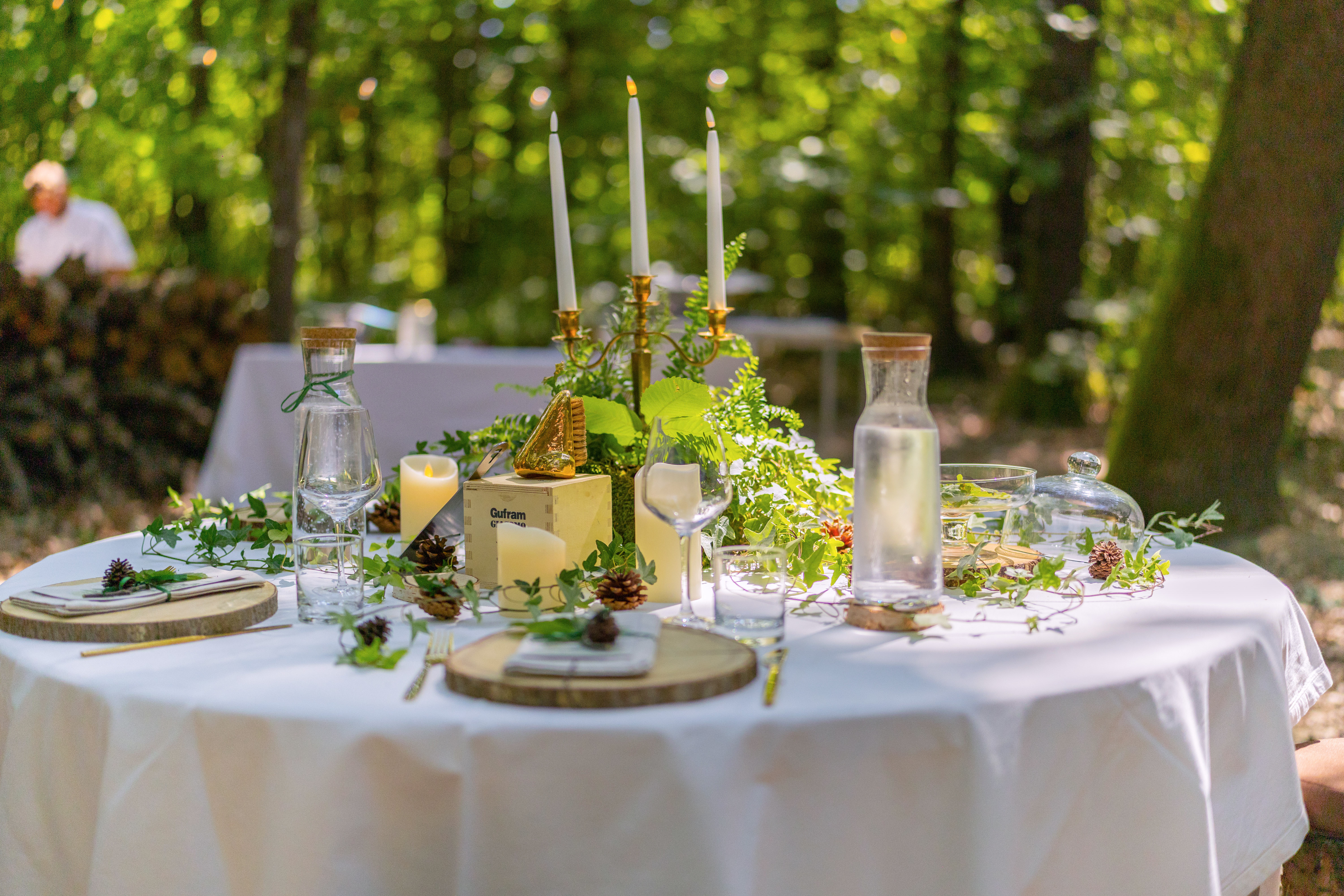 Rustic outdoor dining table with candelabra, greenery, candles in forest.