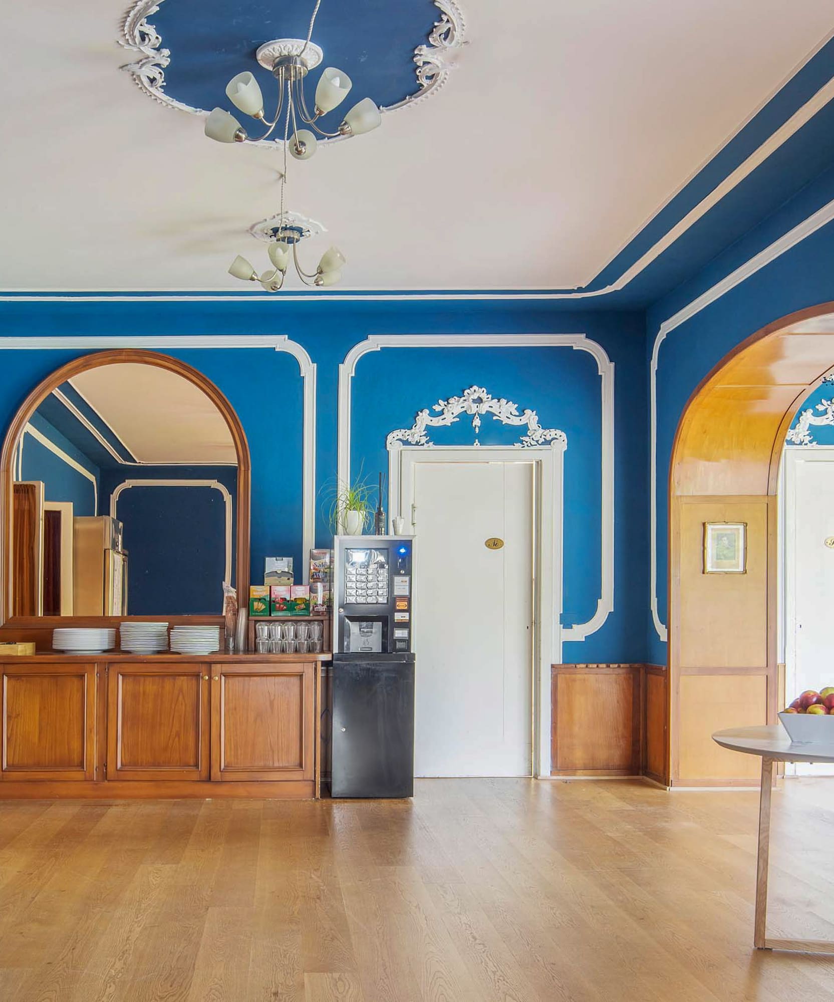 Ornate blue room with white trim, hardwood floor, coffee station, and mirror.