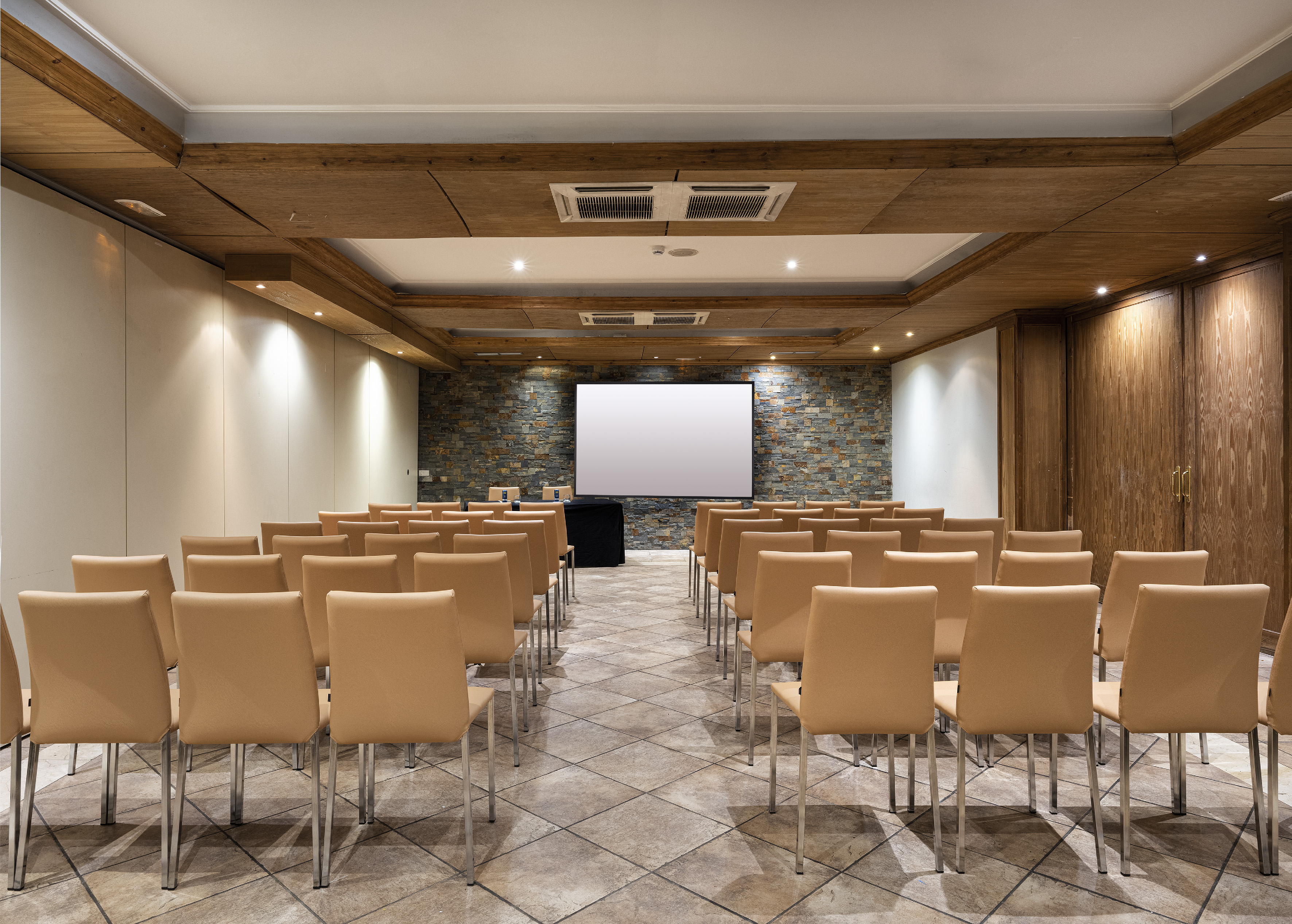 Conference room with tan chairs, large projection screen, stone wall, wood ceiling.