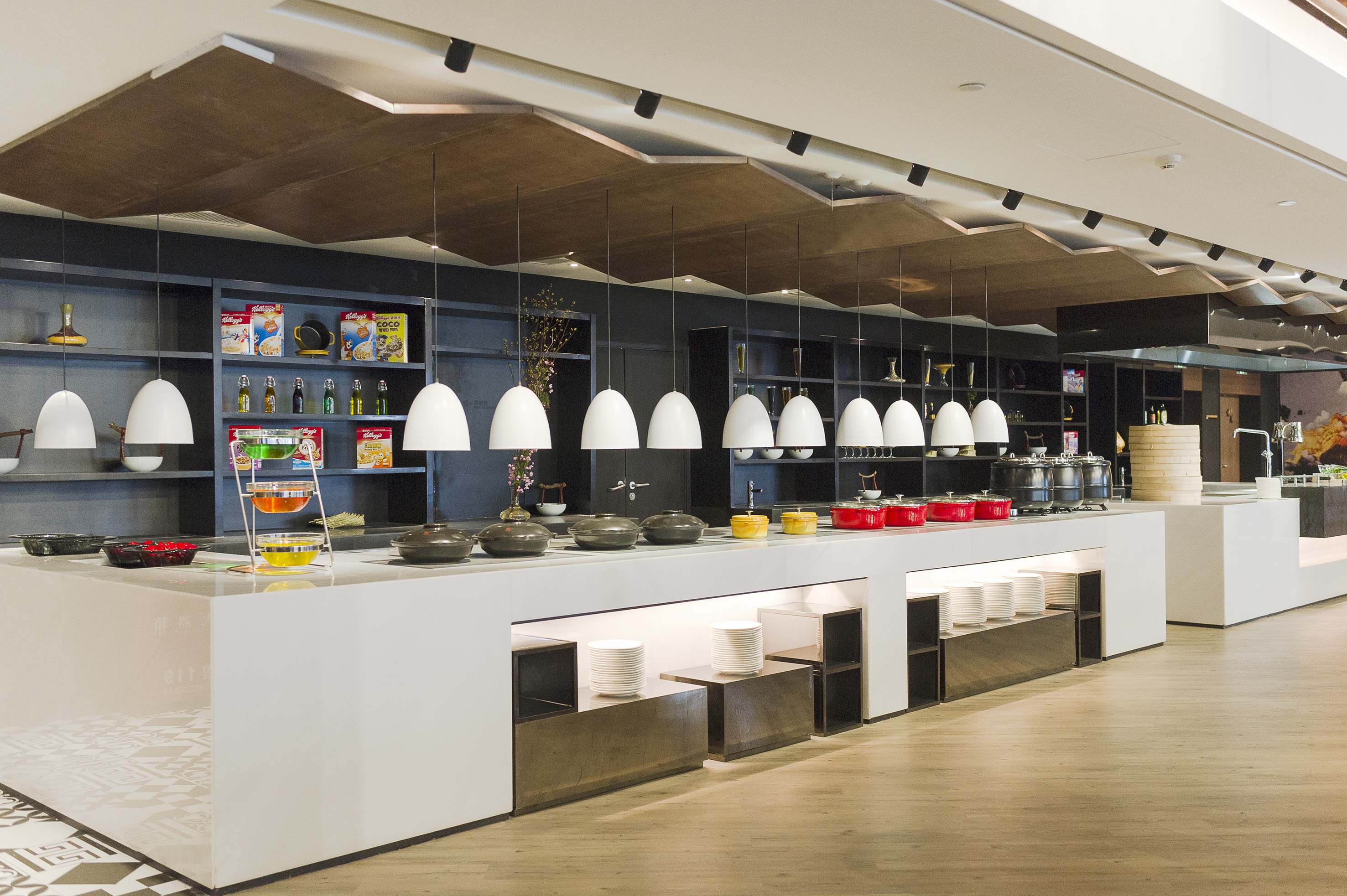 Modern hotel buffet with multiple serving stations, pendant lights, and food displays.