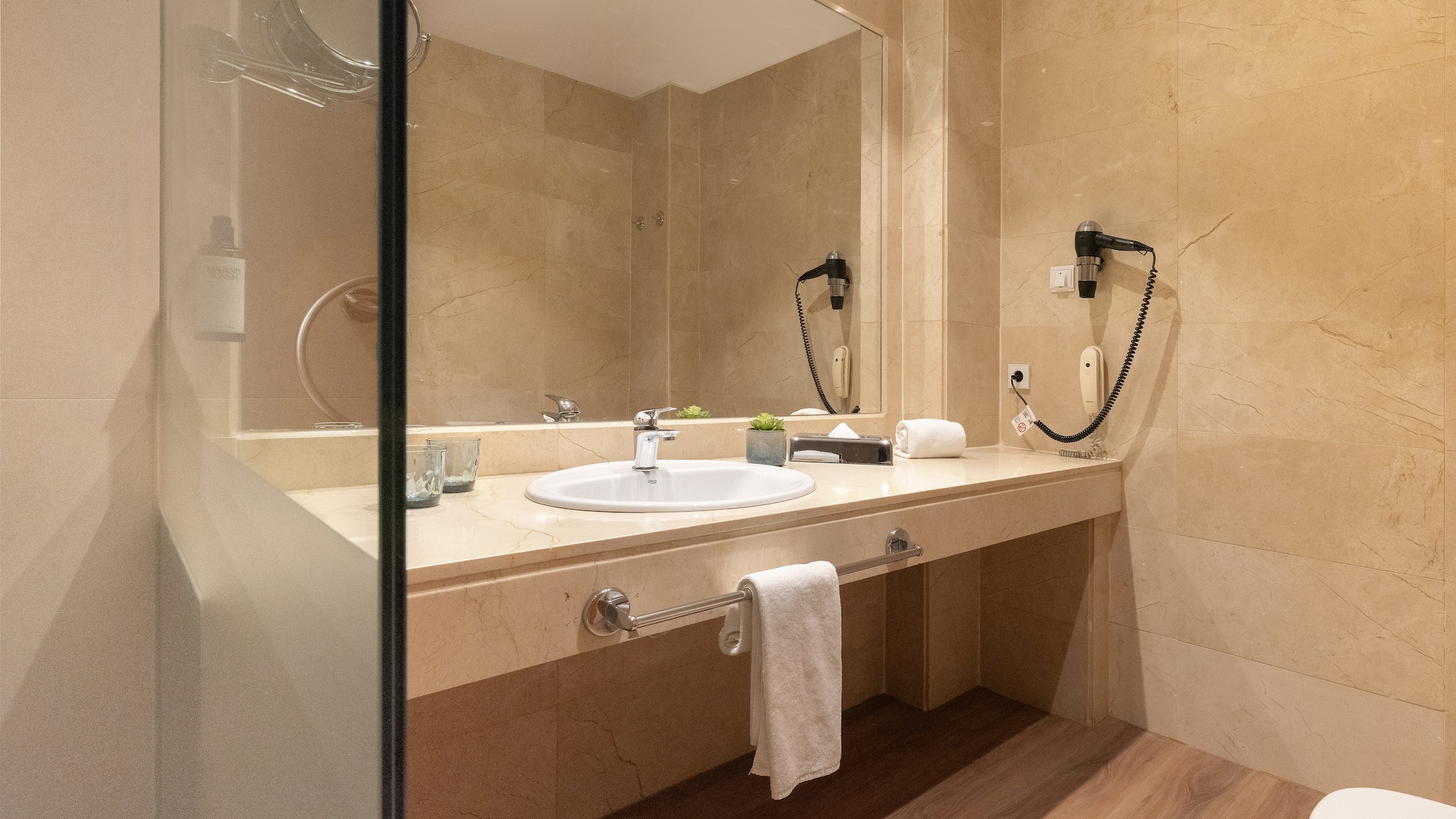 Modern hotel bathroom with marble vanity, sink, mirror, and hairdryer.
