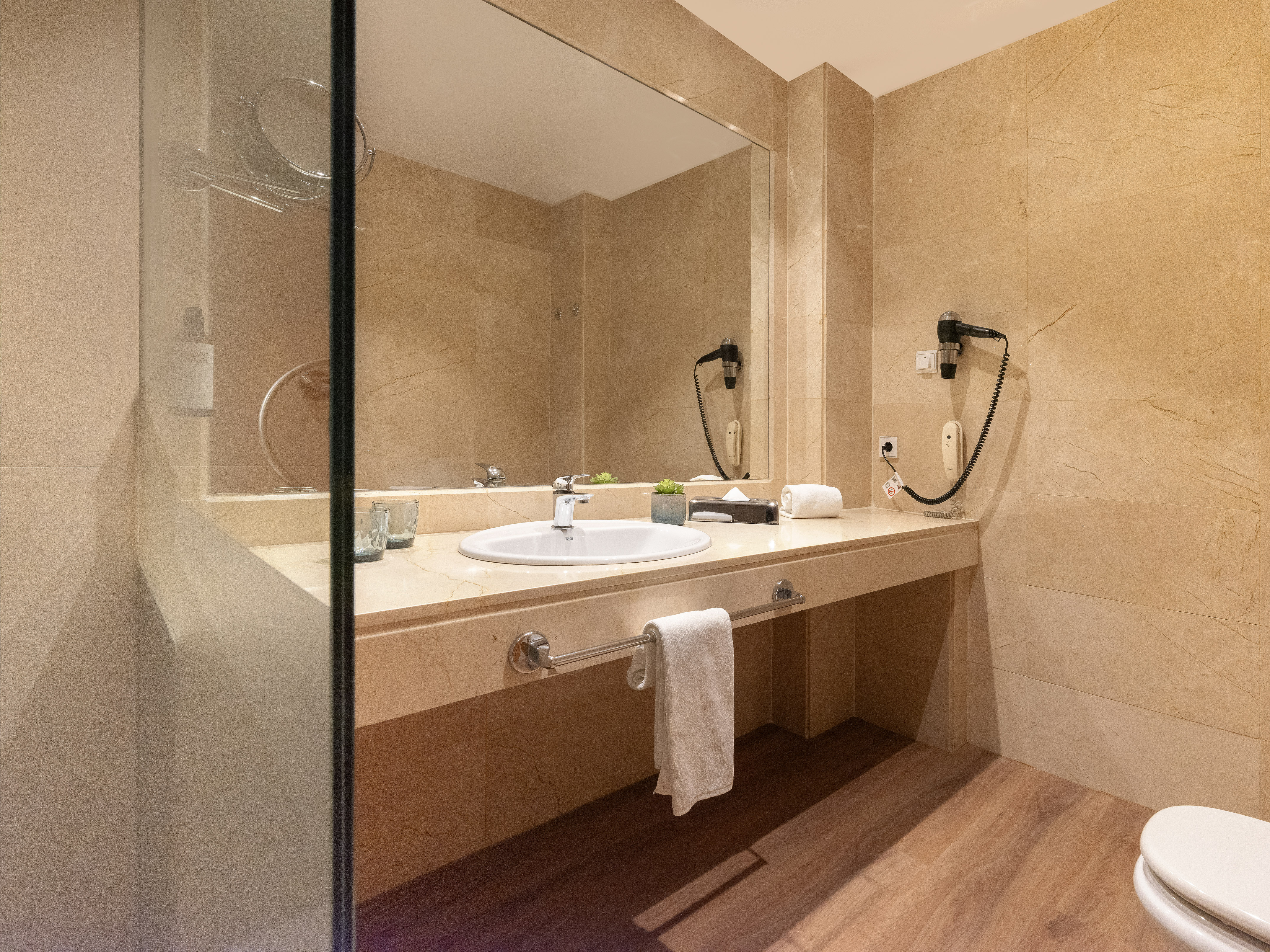 Modern hotel bathroom with marble vanity, sink, mirror, and hairdryer.