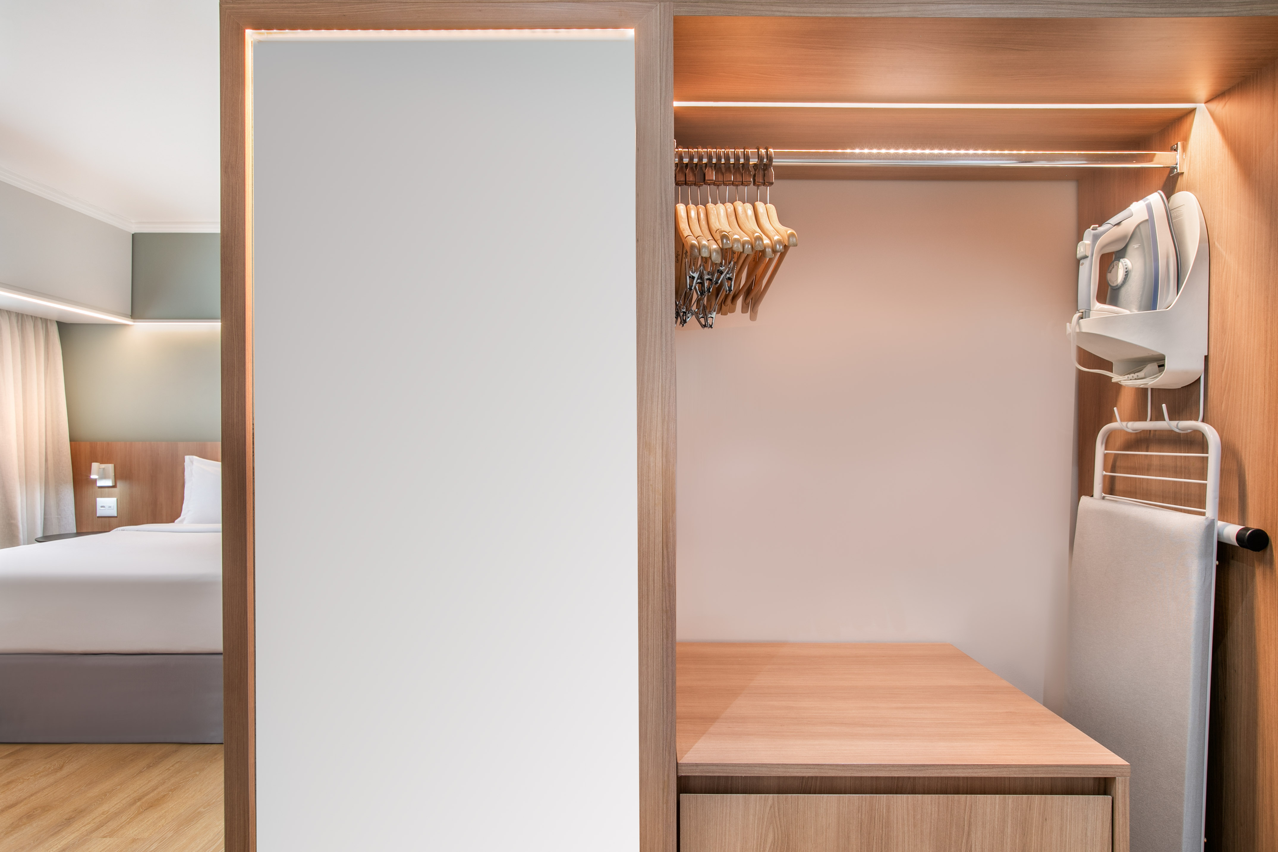 Hotel room closet with iron, ironing board, and hangers. Modern design.
