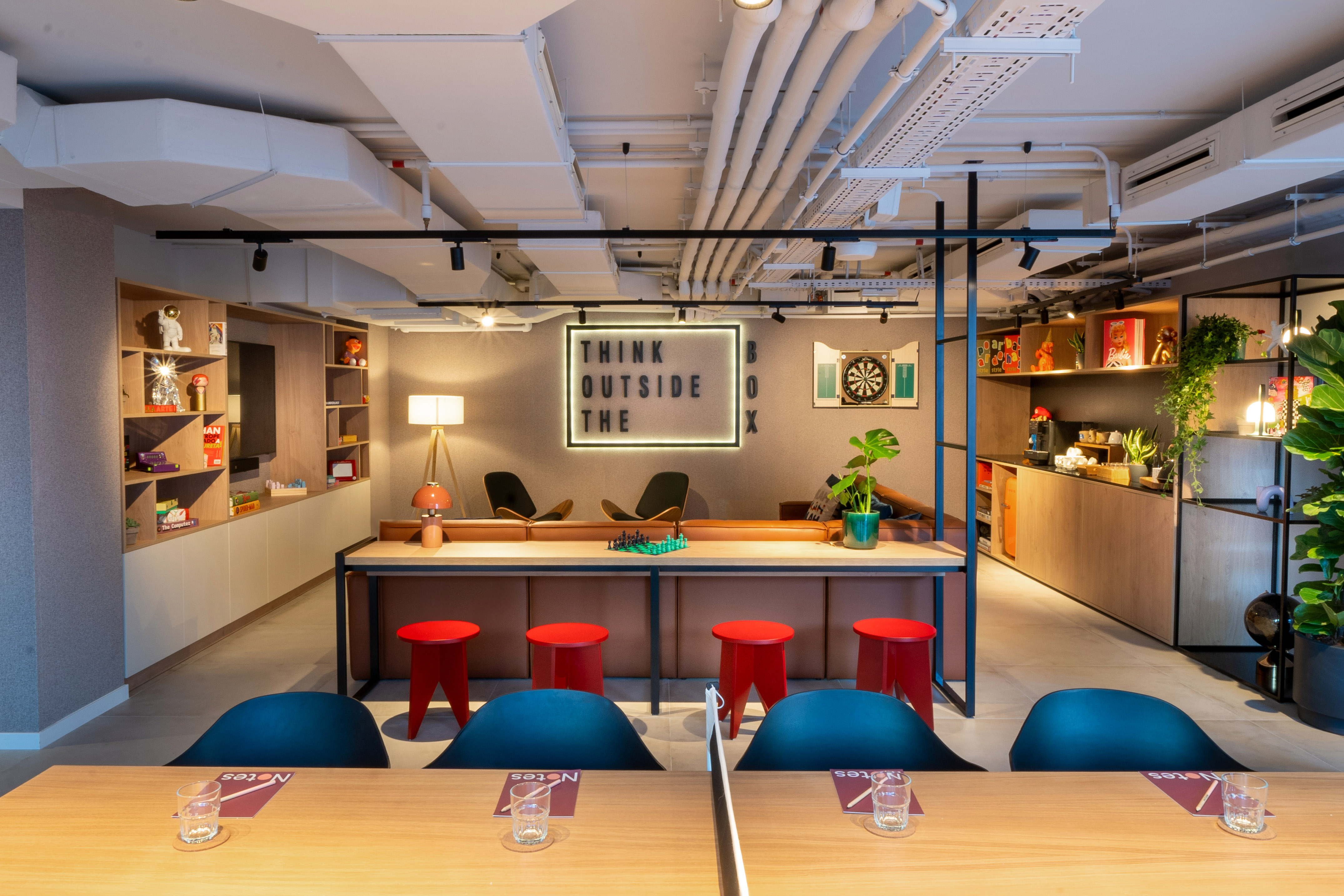 Modern coworking lounge with "Think Outside The Box" sign, dartboard, and seating areas.